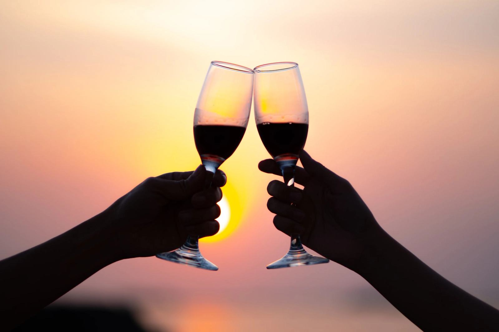 Two wine glasses raised against the sunset over the sea.