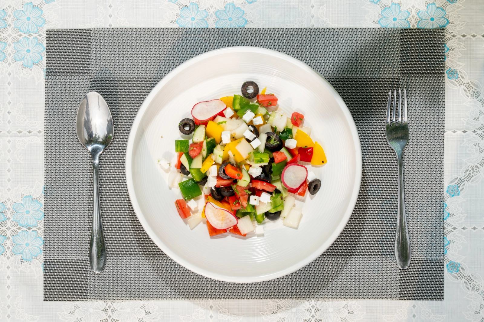 Overhead view of a colourful salad on a white plate with neatly arranged cutlery.