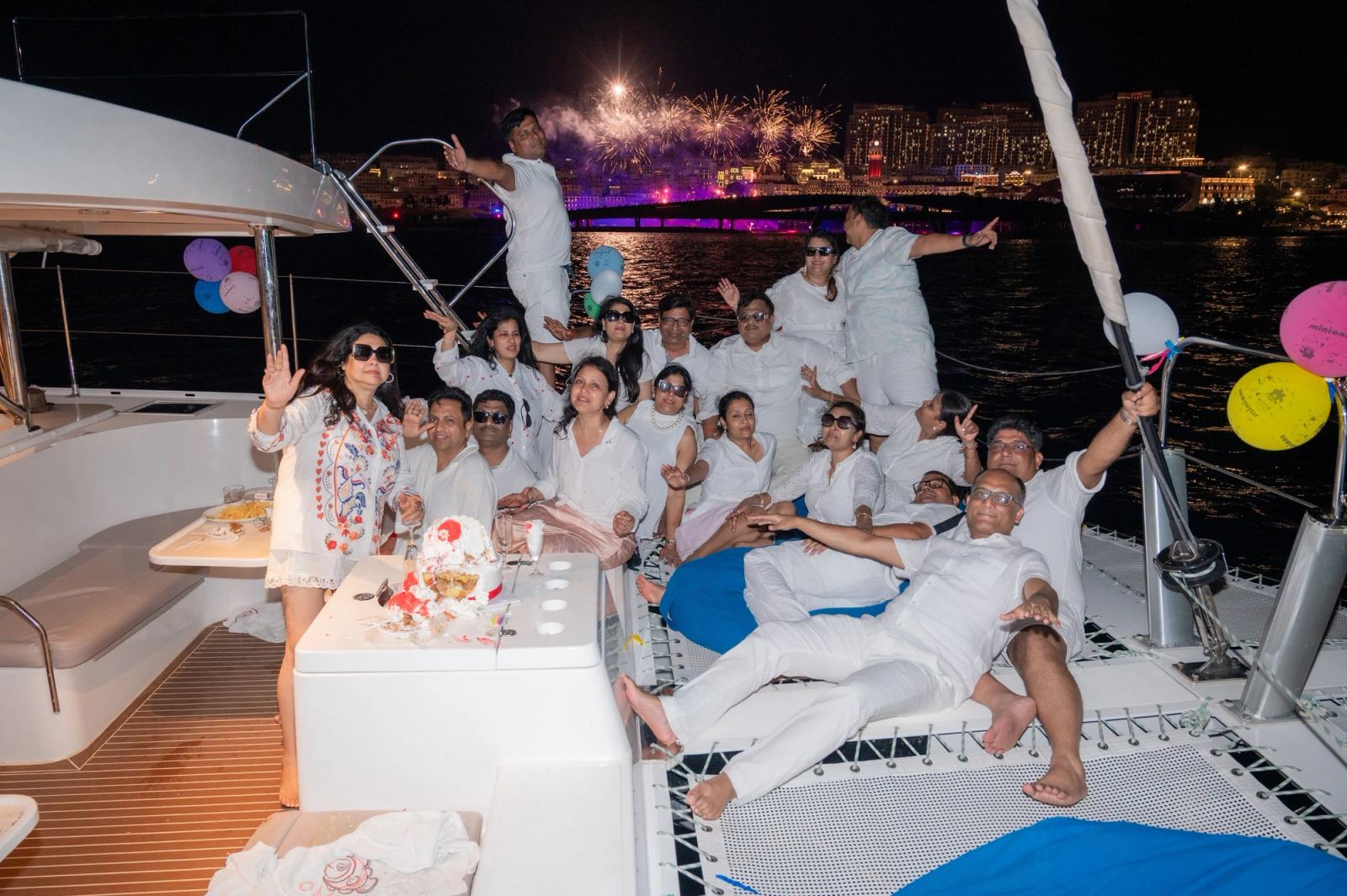 Guests posing on a yacht as fireworks light up the waterfront behind them.