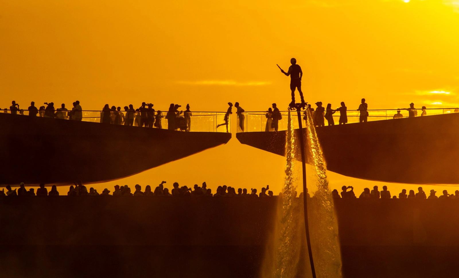 Silhouette of a water-powered performer above the sea beside spectators on Kiss Bridge.