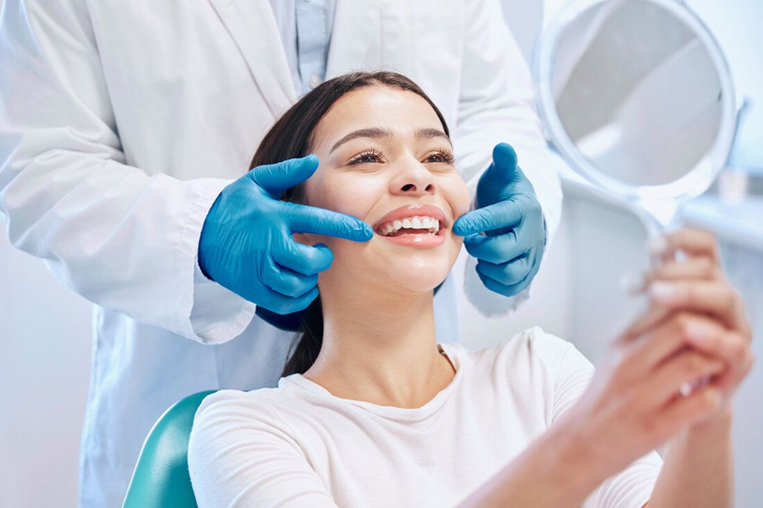 Woman in dental chair looks in mirror and admires her white teeth after teeth-whitening in San Francisco