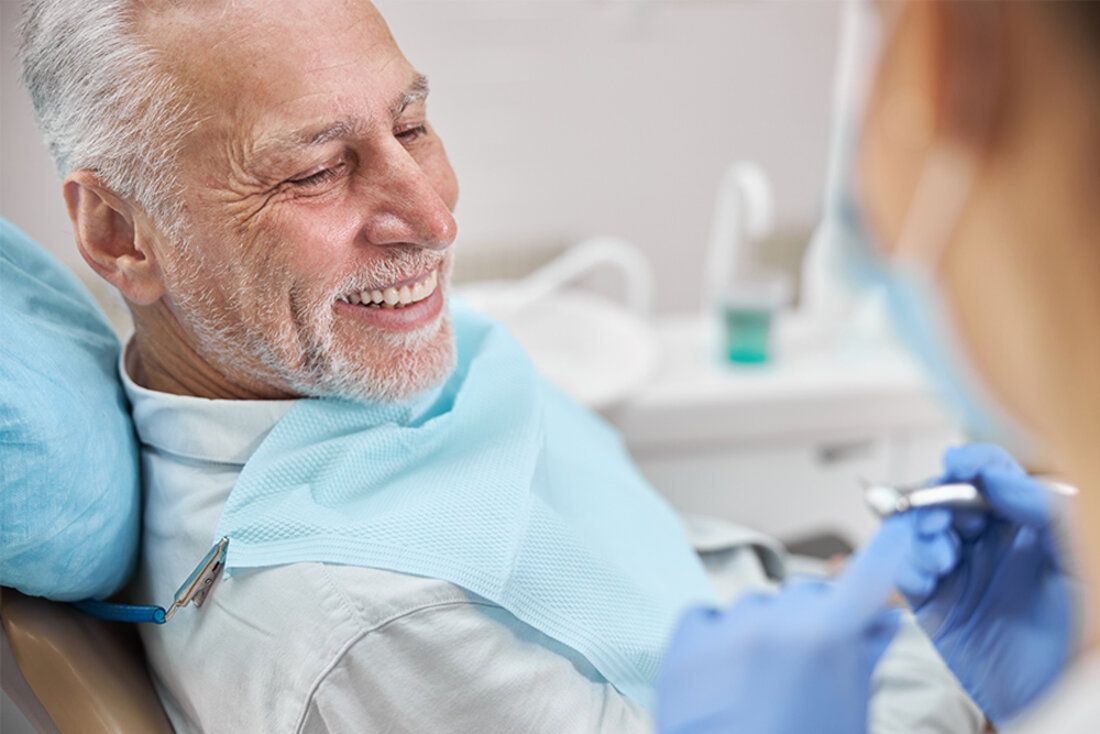 Handsome, senior man with healthy, white teeth smiles into mirror after getting veneers with the best cosmetic dentist in San Francisco