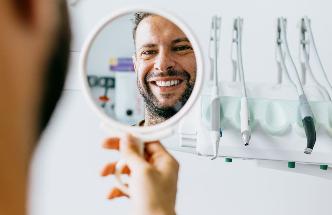 Handsome man with healthy, white teeth looks into mirror and smiles after treatment at the highest-rated cosmetic dentist in San Francisco 