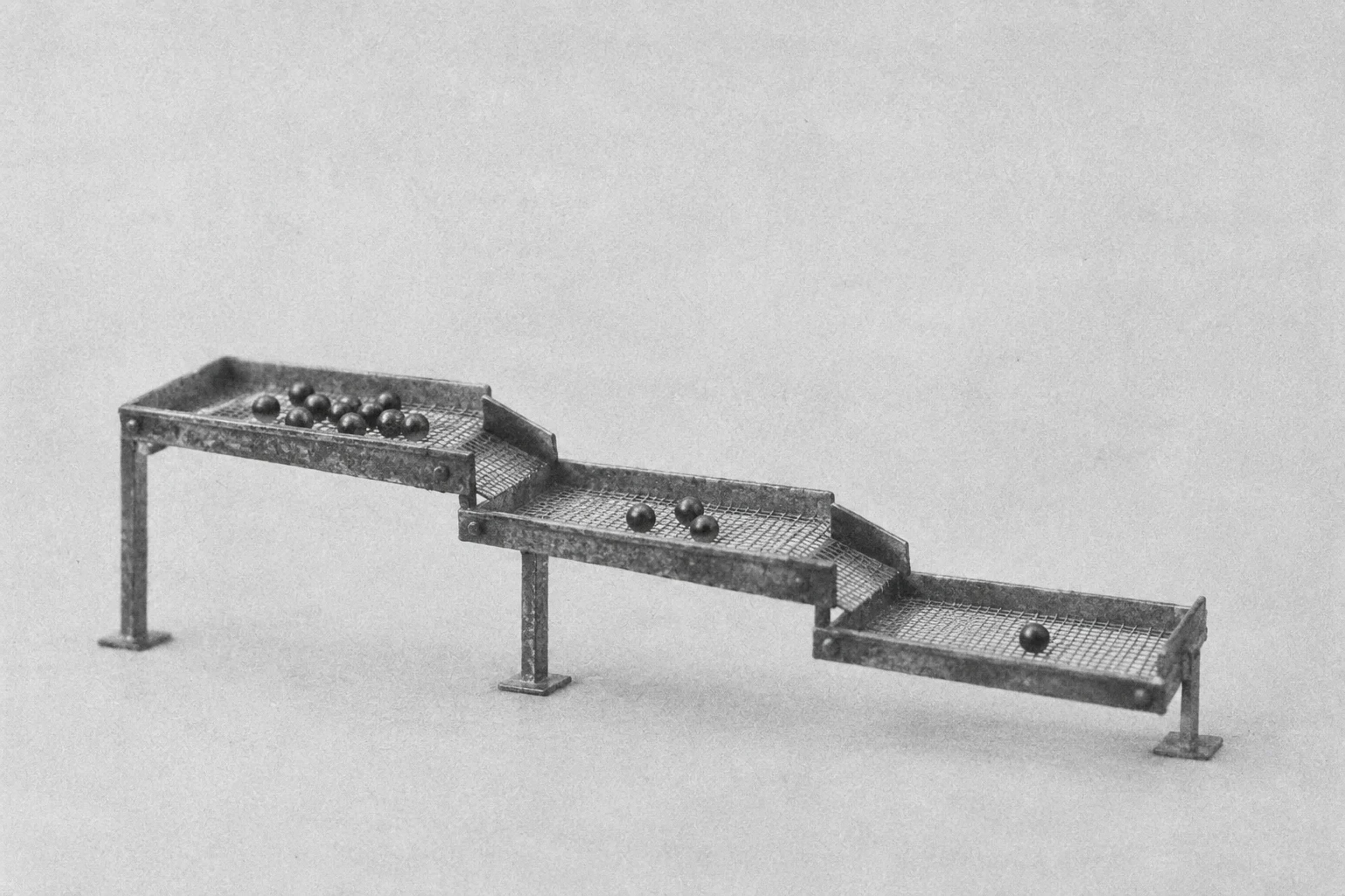 Grainy monochrome illustration of three successive sorting trays holding progressively fewer steel balls.
