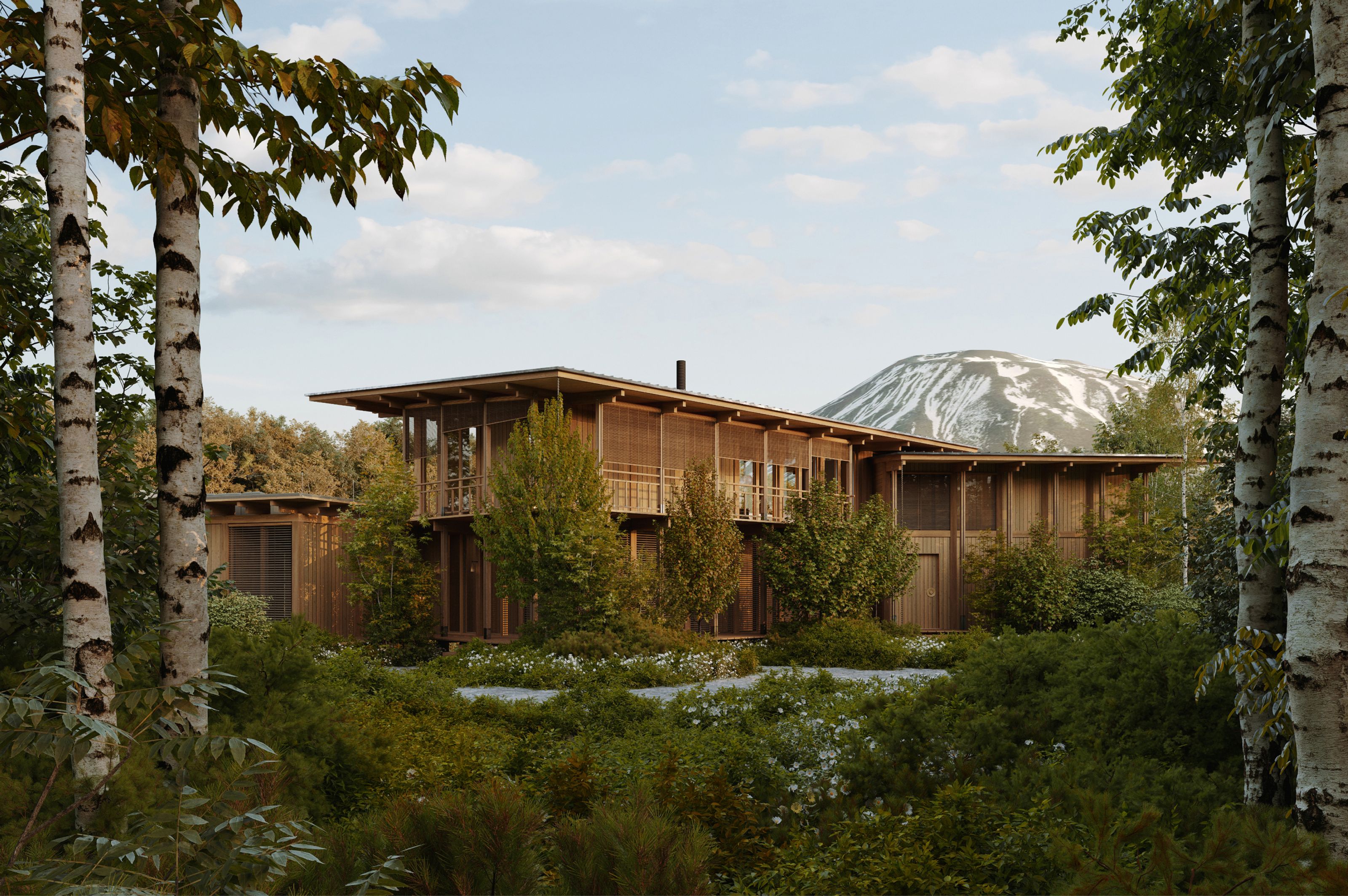 A long, low wooden building surrounded by dense green foliage and birch trees, with a large gray and white mound in the distance.