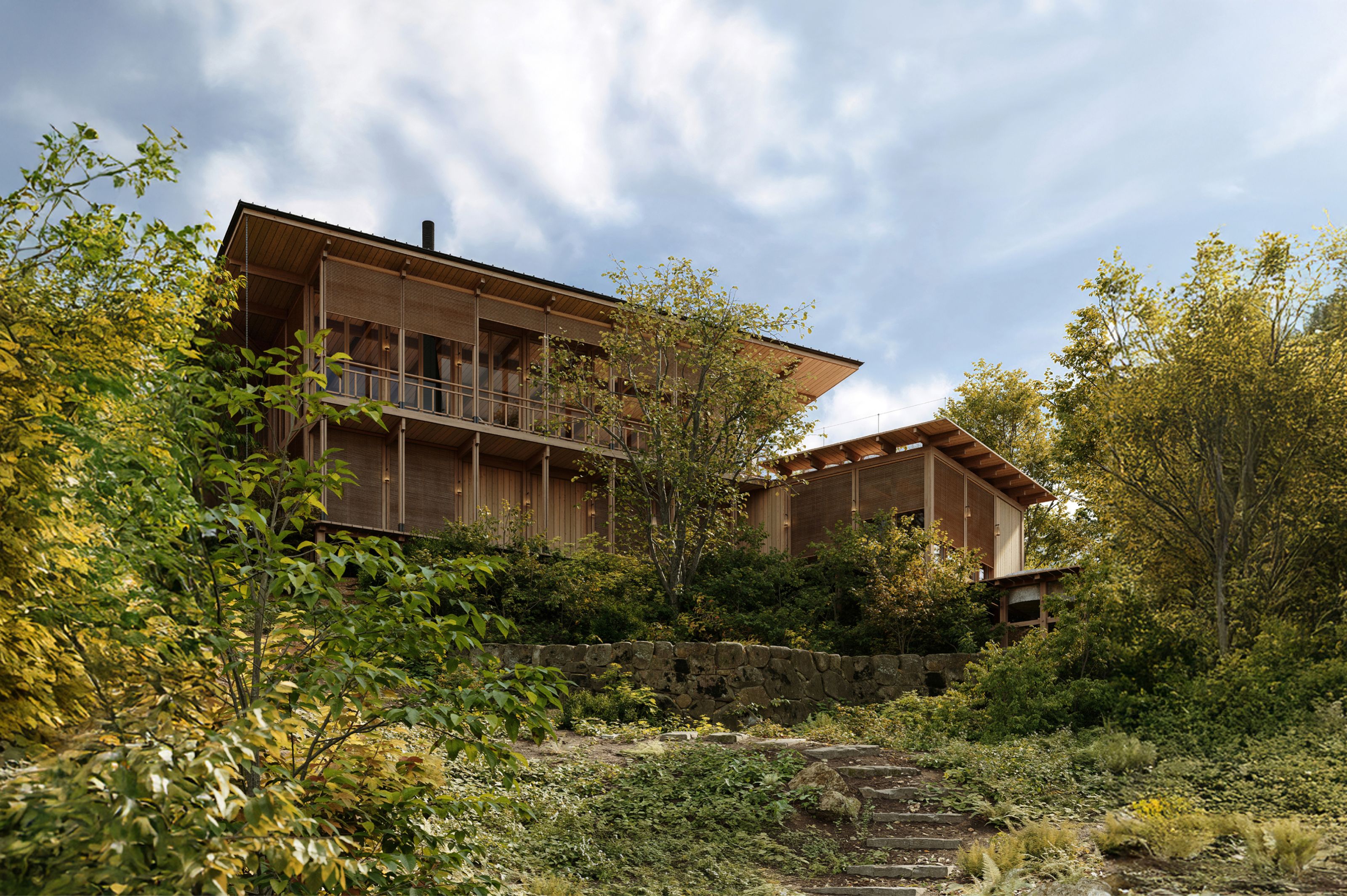 Wooden house with balconies and a smaller building on a lush, tree-covered hillside.