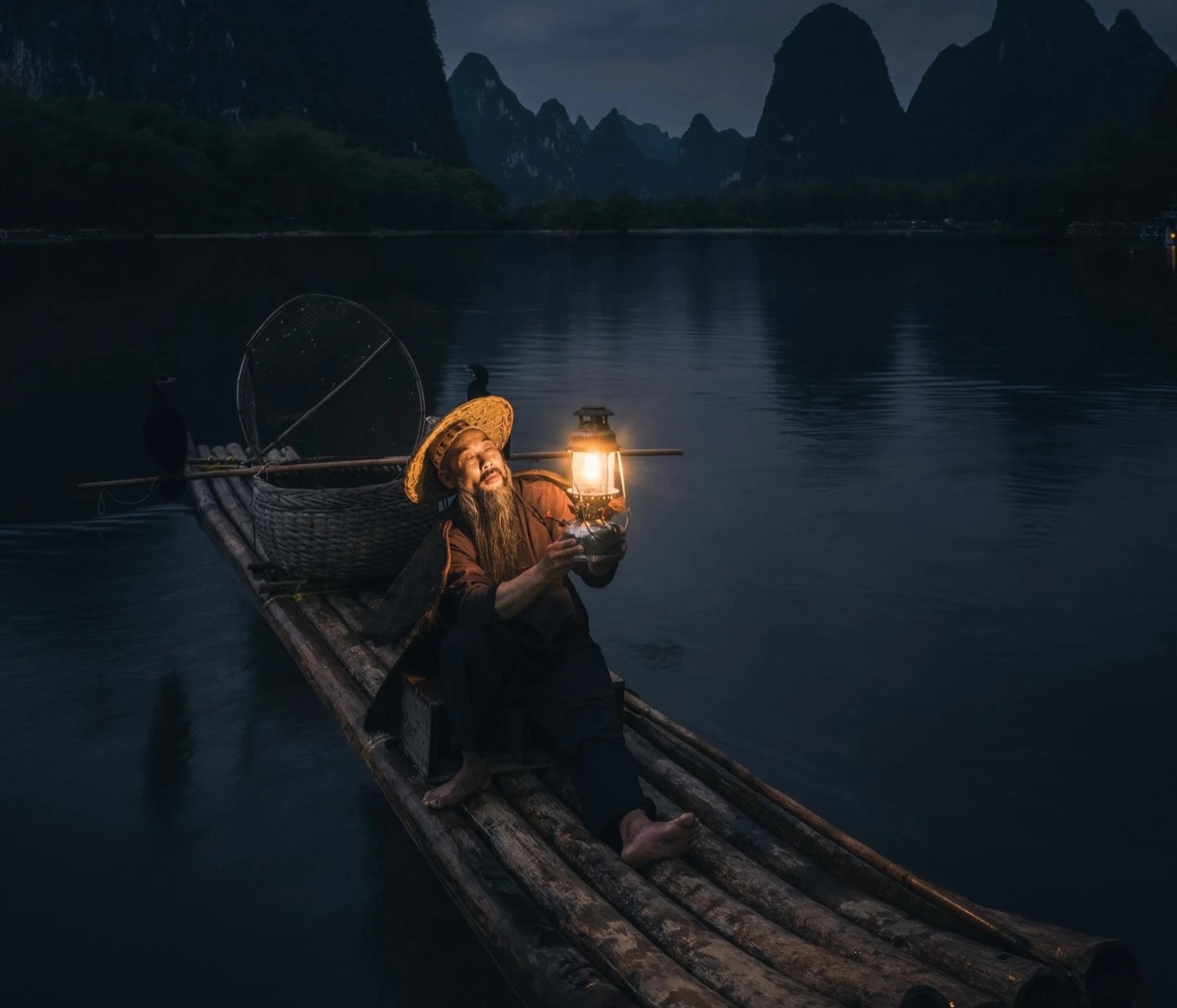 Man on a boat holding a lantern lighting his face. 