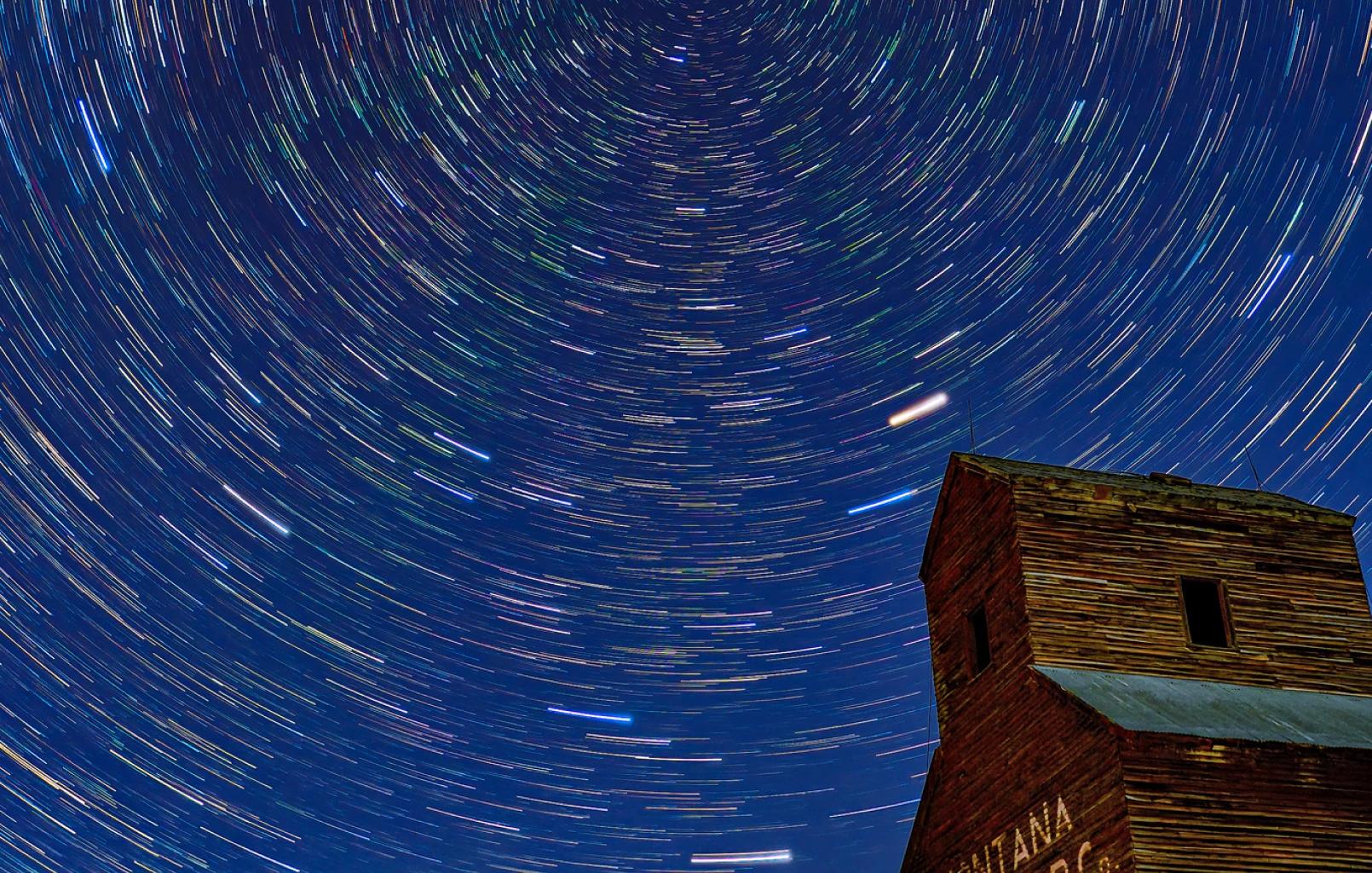 Photo of star trails with a Montana ranch home in the lower right corner.