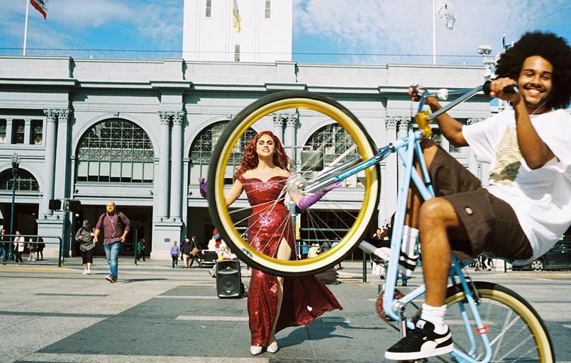 Bike doing a wheelie with a girl in the background between the inside of the front tire.