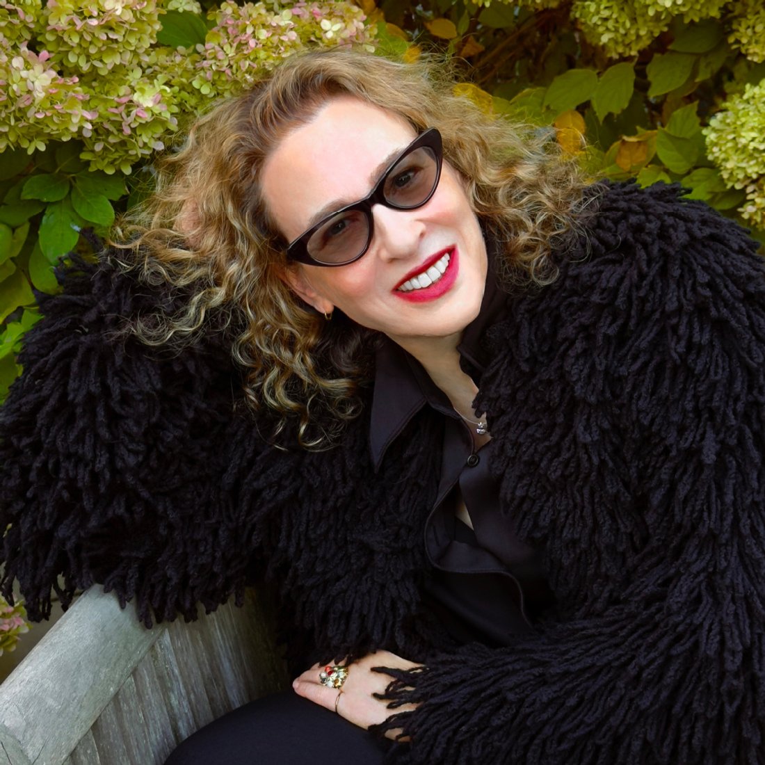BioFur founder Kym Canter wearing a fax fur jacket, sunglasses, and red lipstick, smiling at the camera