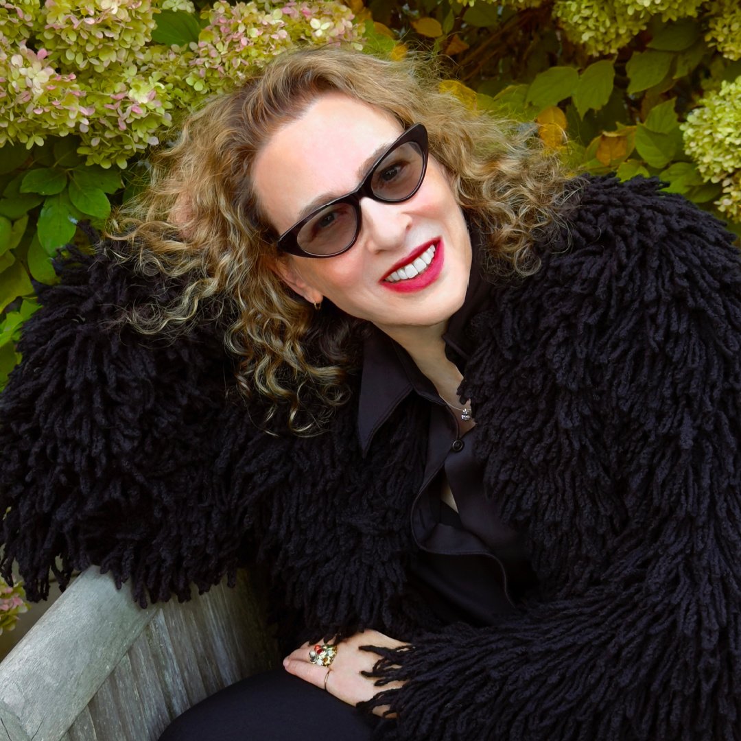 BioFur founder Kym Canter wearing a fax fur jacket, sunglasses, and red lipstick, smiling at the camera