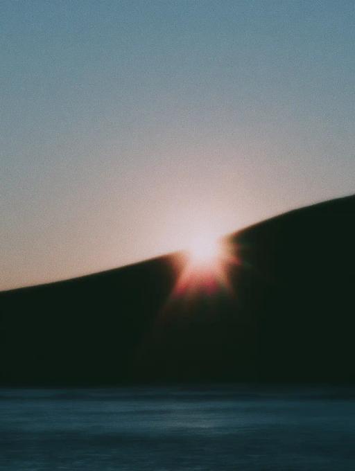 Sol brillante asomándose entre dos colinas oscuras sobre un lago tranquilo al amanecer.