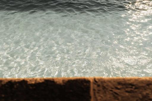 Agua clara con reflejos de luz y borde inferior de piedra marrón desenfocada.