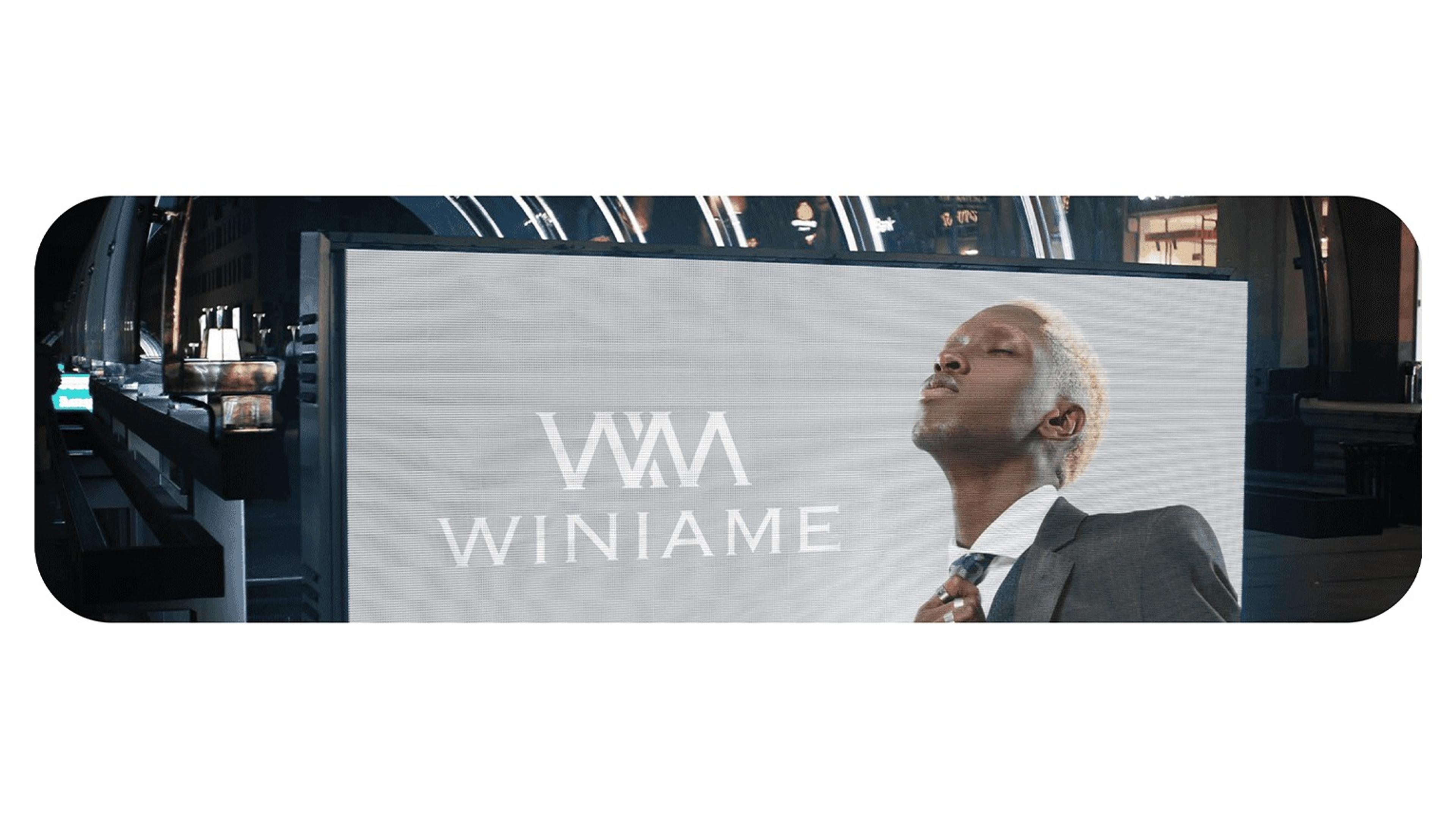 Winiame logo on a large screen beside a model in a suit