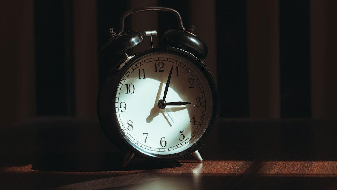 A vintage alarm clock sits on a wooden surface - Photo by Suhas Hanjar on Unsplash