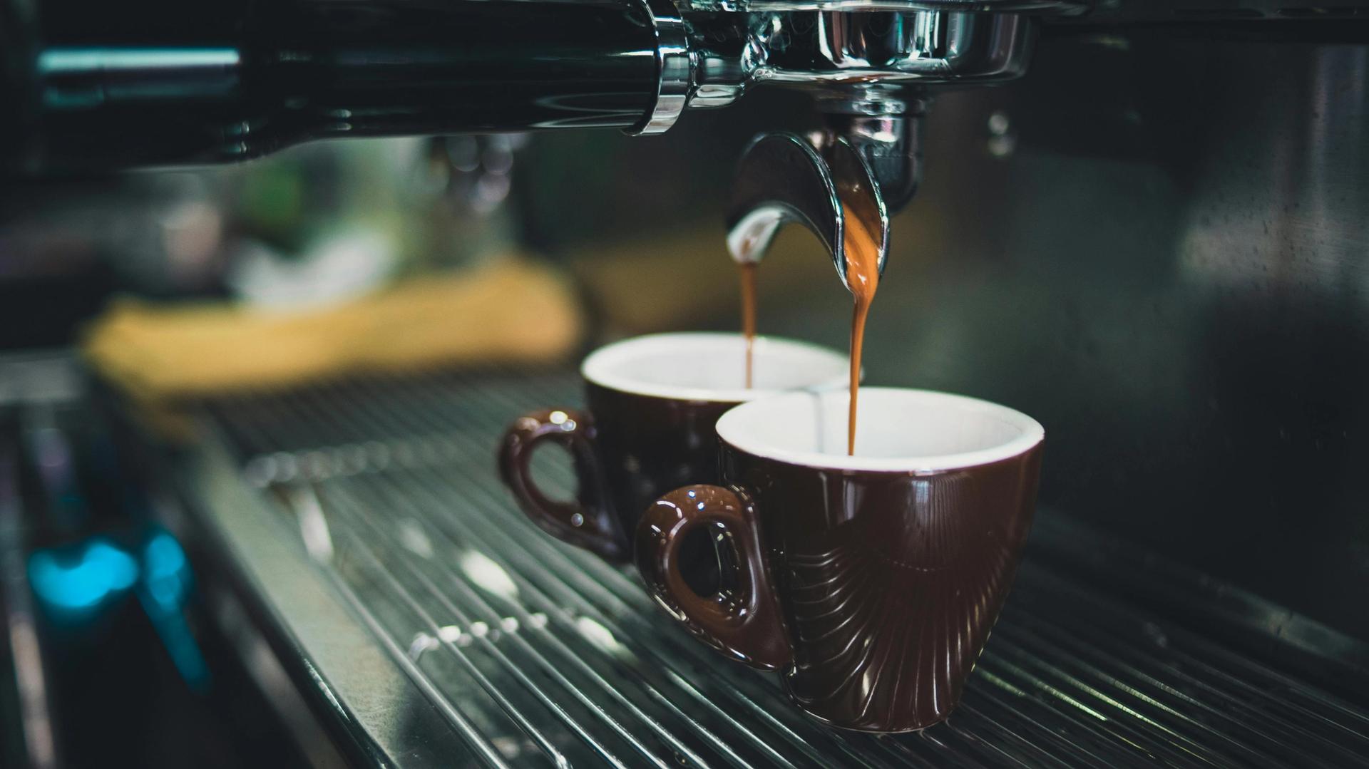 Two cups of coffee are being poured into a coffee machine