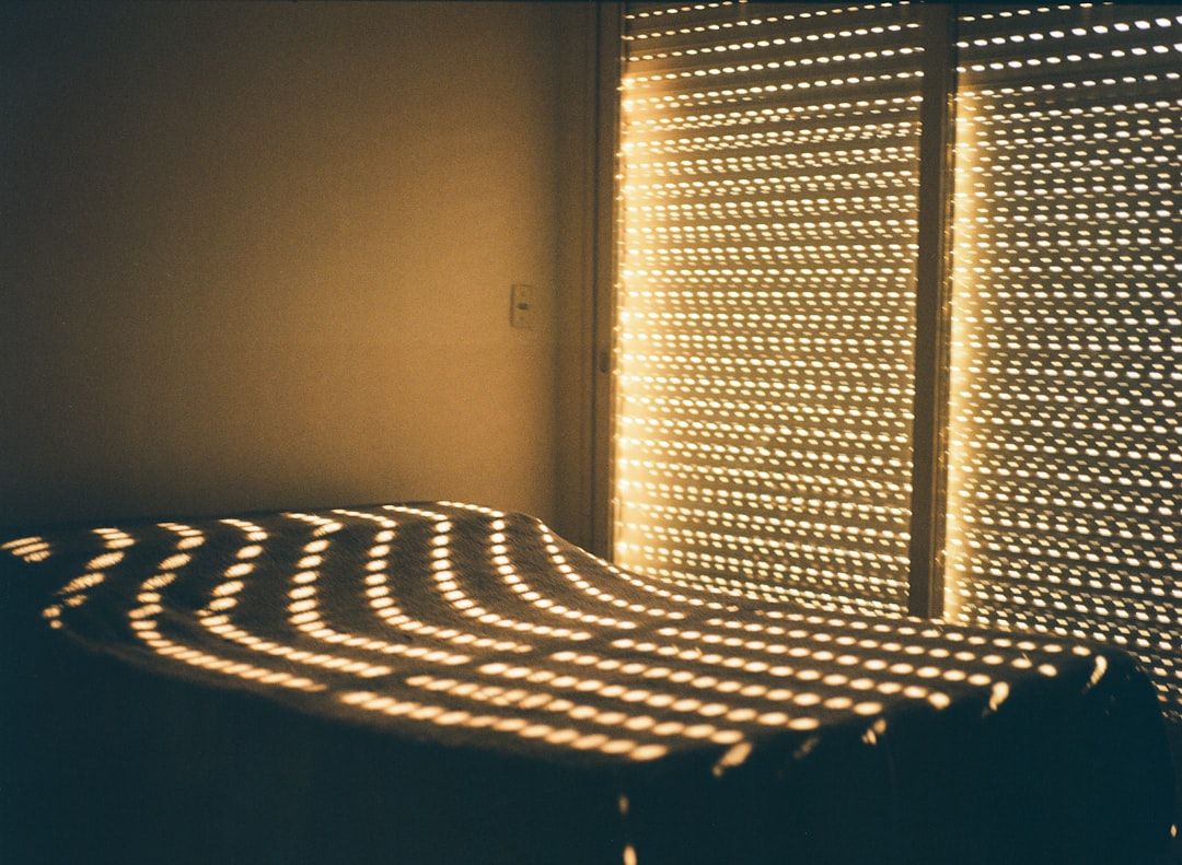 Warm sunlight filtering through blinds casts nostalgic patterns across an unmade bed, creating a quiet, intimate moment filled with memory and stillness. - Photo by Ruben Mavarez on Unsplash