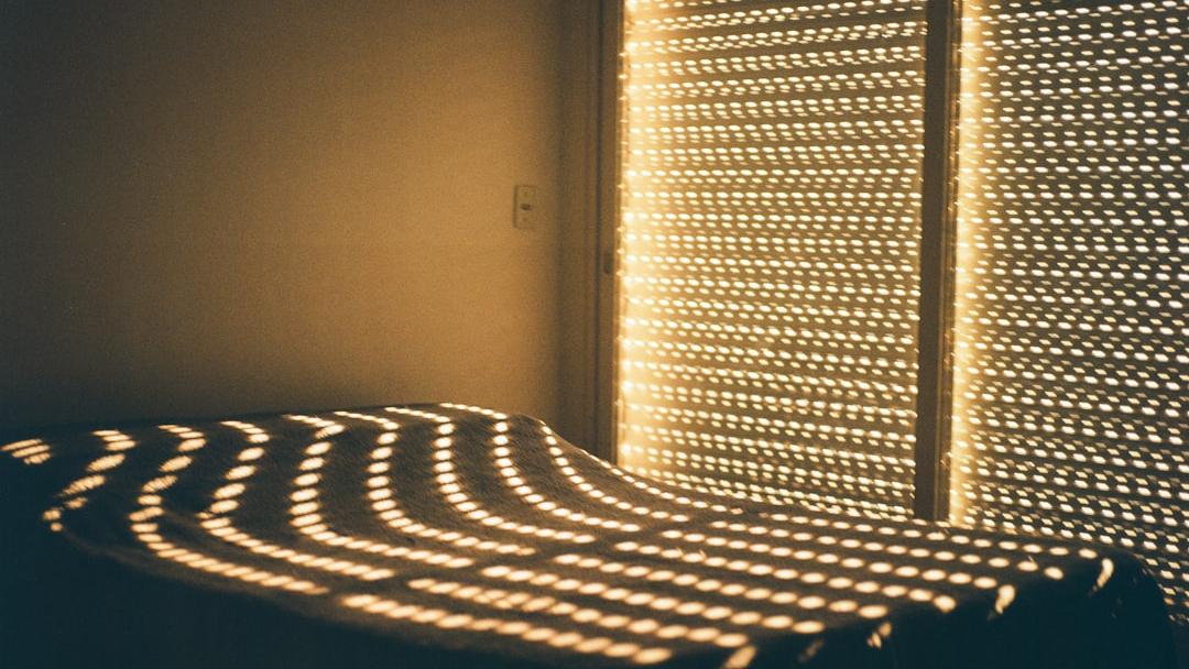 Warm sunlight filtering through blinds casts nostalgic patterns across an unmade bed, creating a quiet, intimate moment filled with memory and stillness. - Photo by Ruben Mavarez on Unsplash
