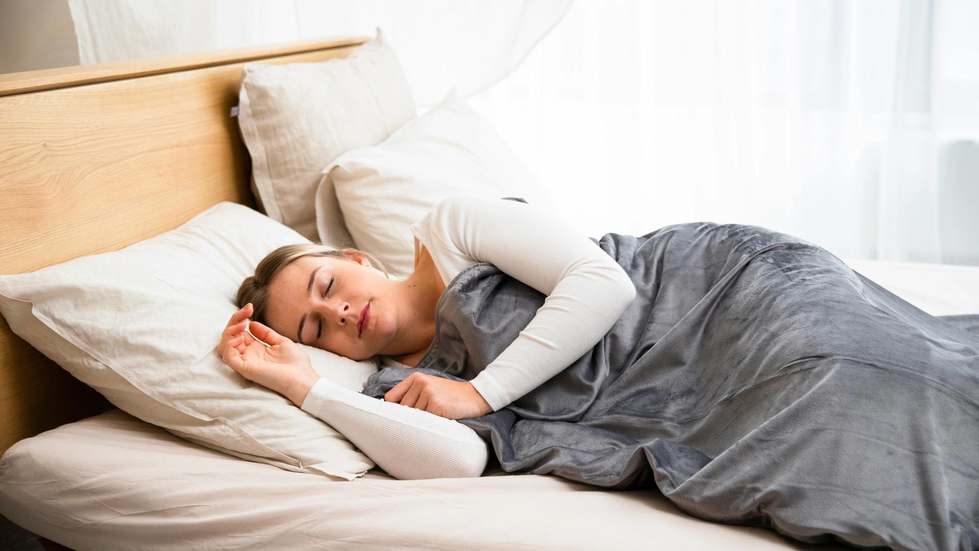 a woman is sleeping on a bed with a weighted blanket .