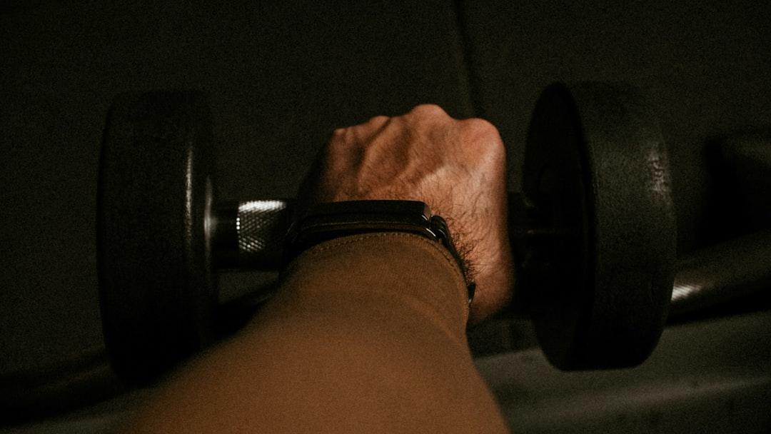 a person's hand holding a barbell in a dark room - Photo by yousef samuil on Unsplash