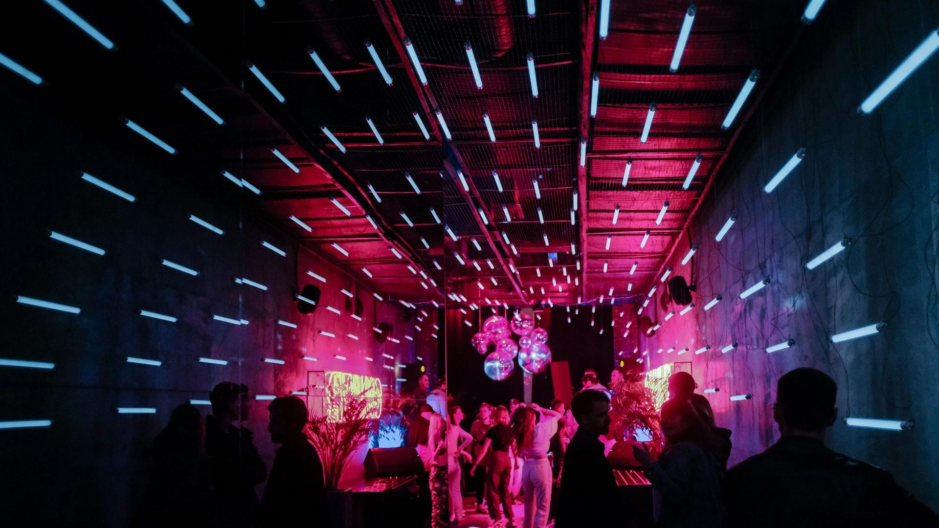 A group of people are dancing in a dark room with neon lights