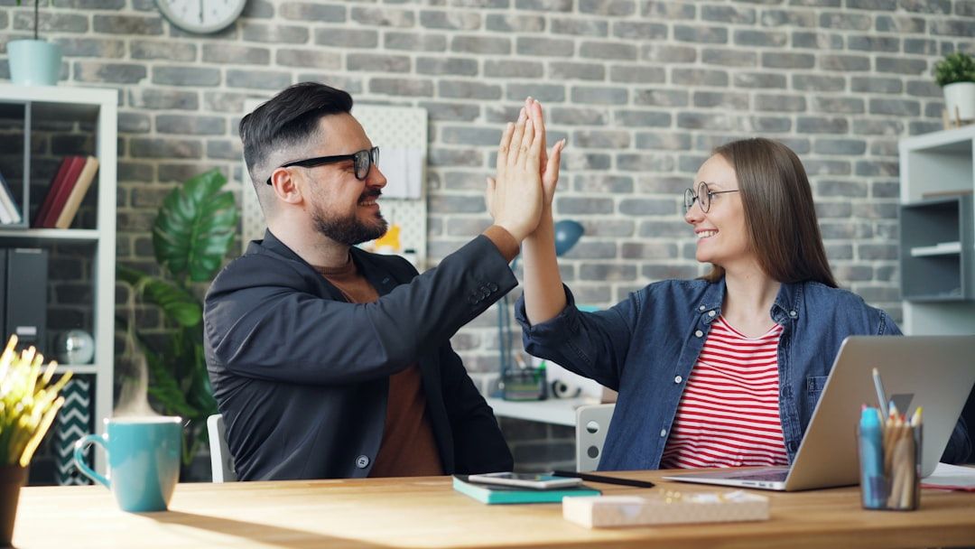 happy colleagues man and woman doing high-five sitting at table in office while cup of hot tea is steaming on desk. People and work concept. - Photo by Vitaly Gariev on Unsplash