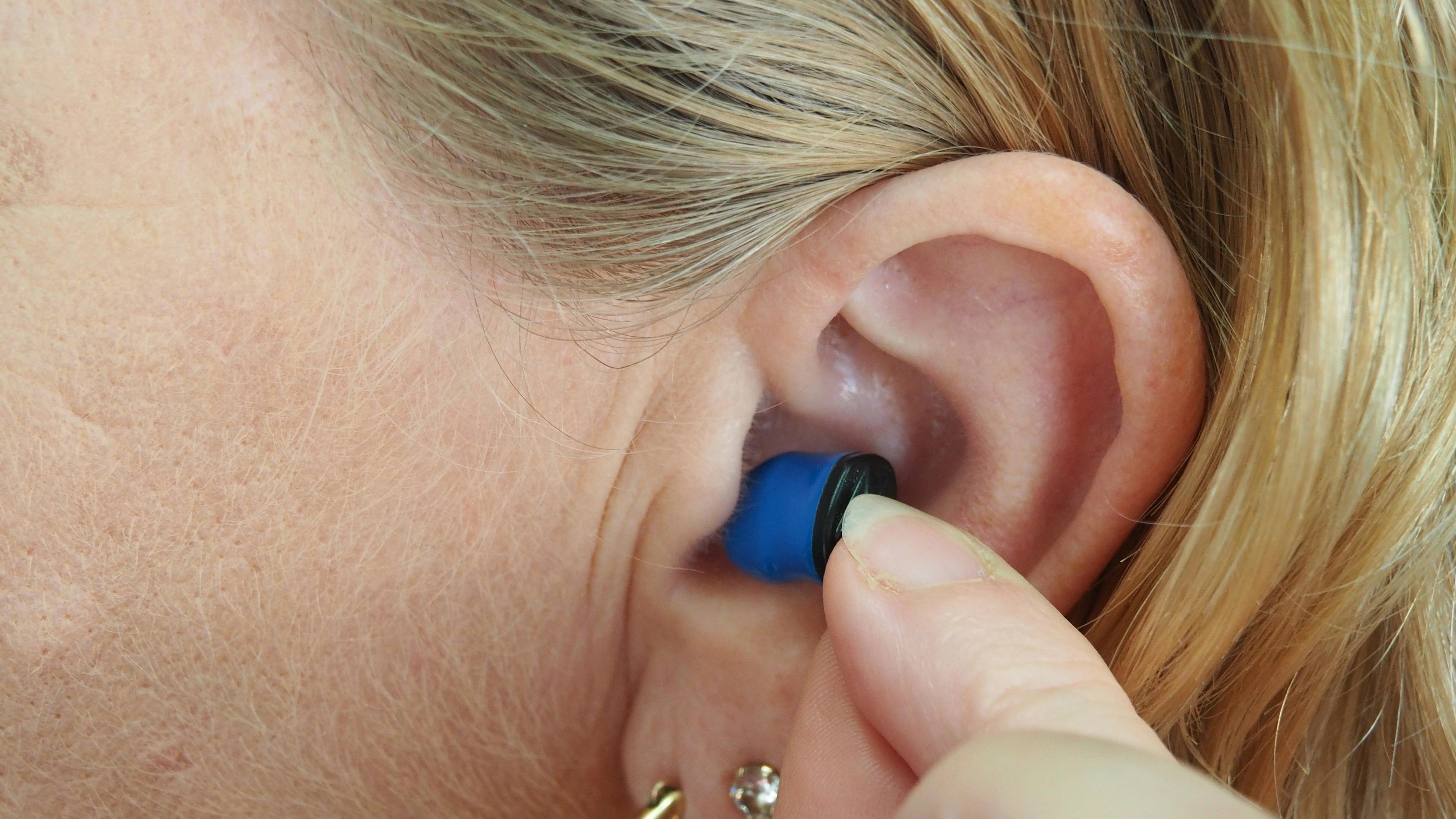 A woman is putting a blue ear plug in her ear
