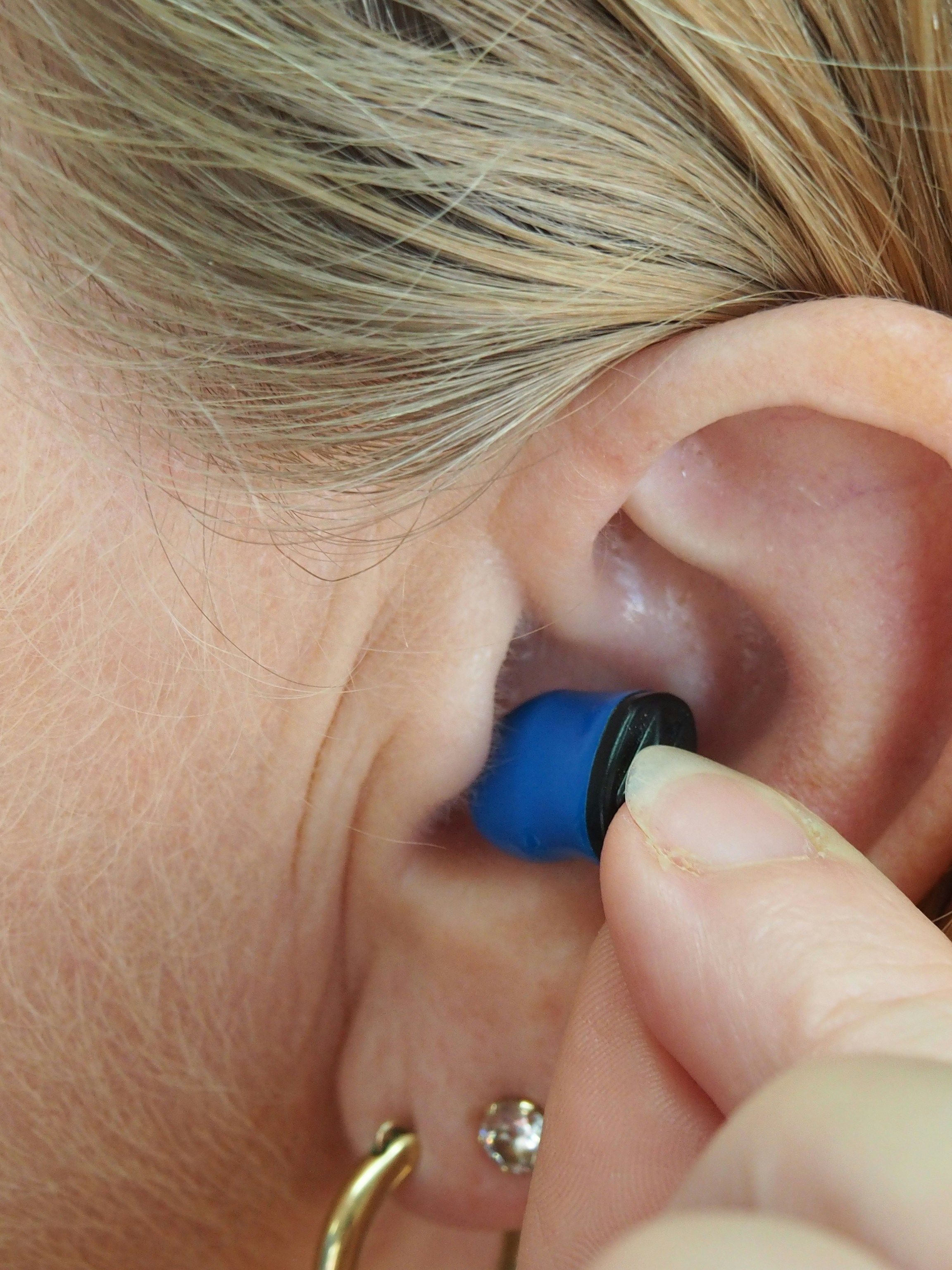 A woman is putting a blue ear plug in her ear
