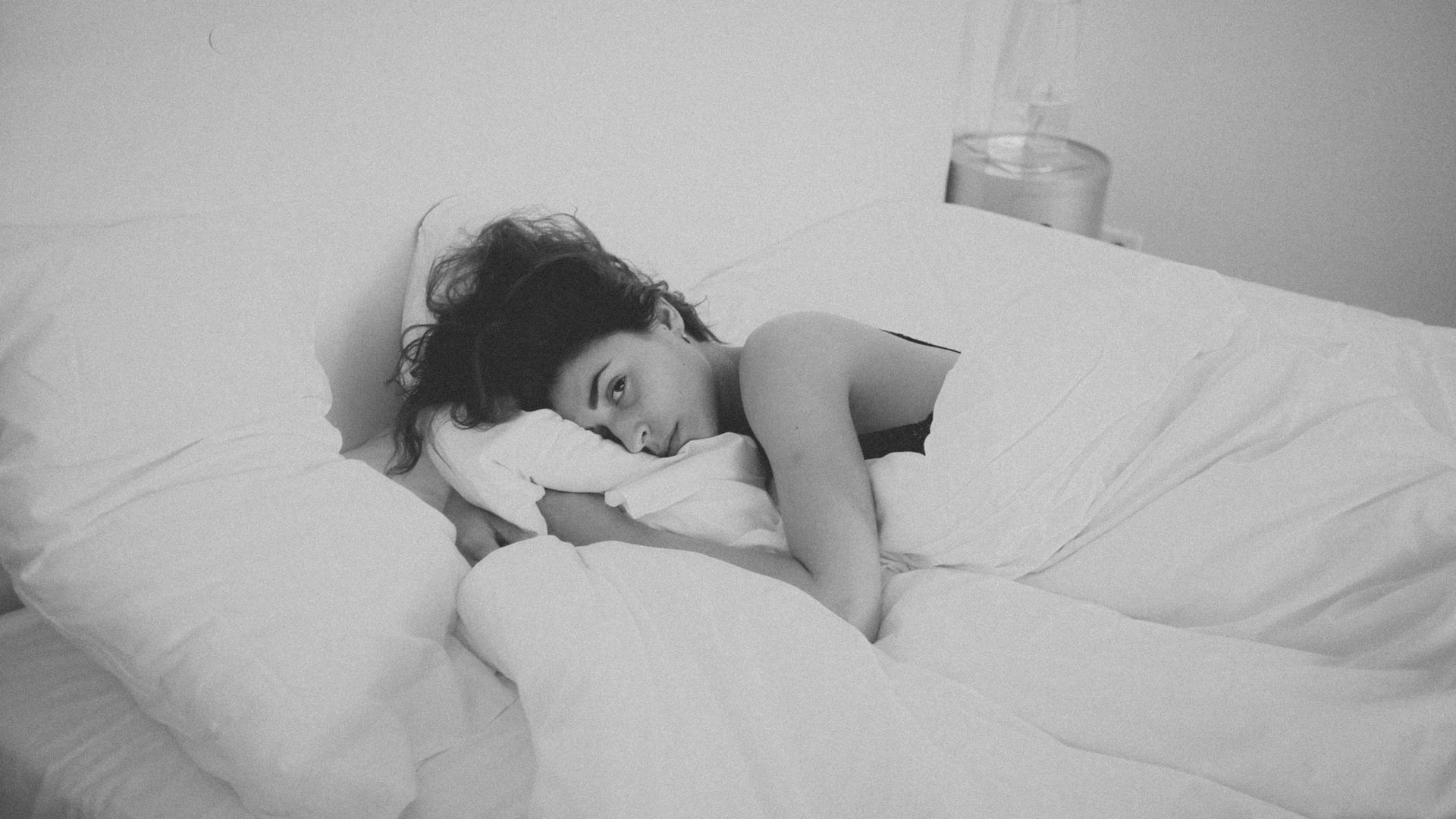 a woman is sleeping in a bed with white sheets and pillows .