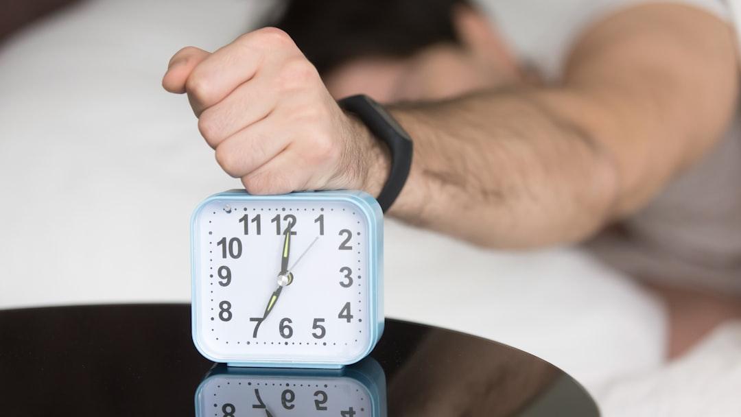 A man laying in bed with a clock on top of him - Photo by Solving Healthcare on Unsplash