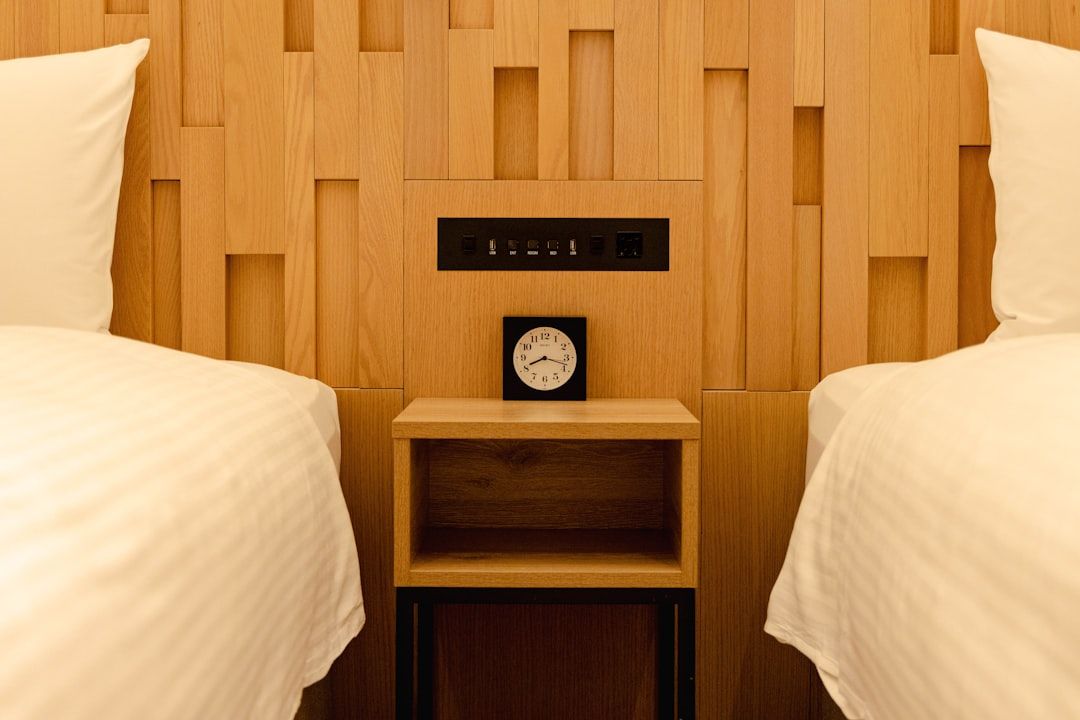 Two beds with a nightstand and clock between them. - Photo by Simon N on Unsplash