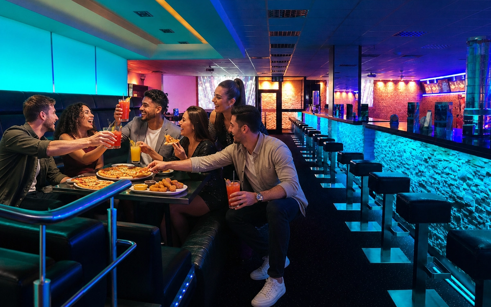 A group shares pizza, snacks and drinks in a blue-lit seating area.