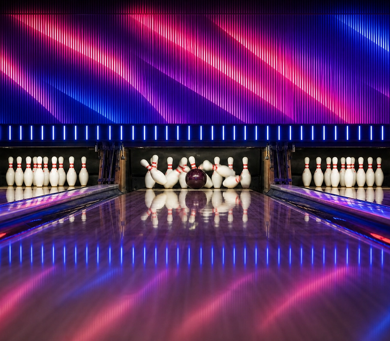 A bowling ball hits the pins in front of a red-and-blue LED wall.