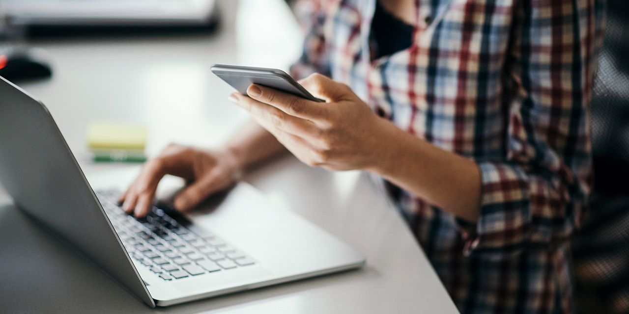 A person using a smartphone and laptop. Photo