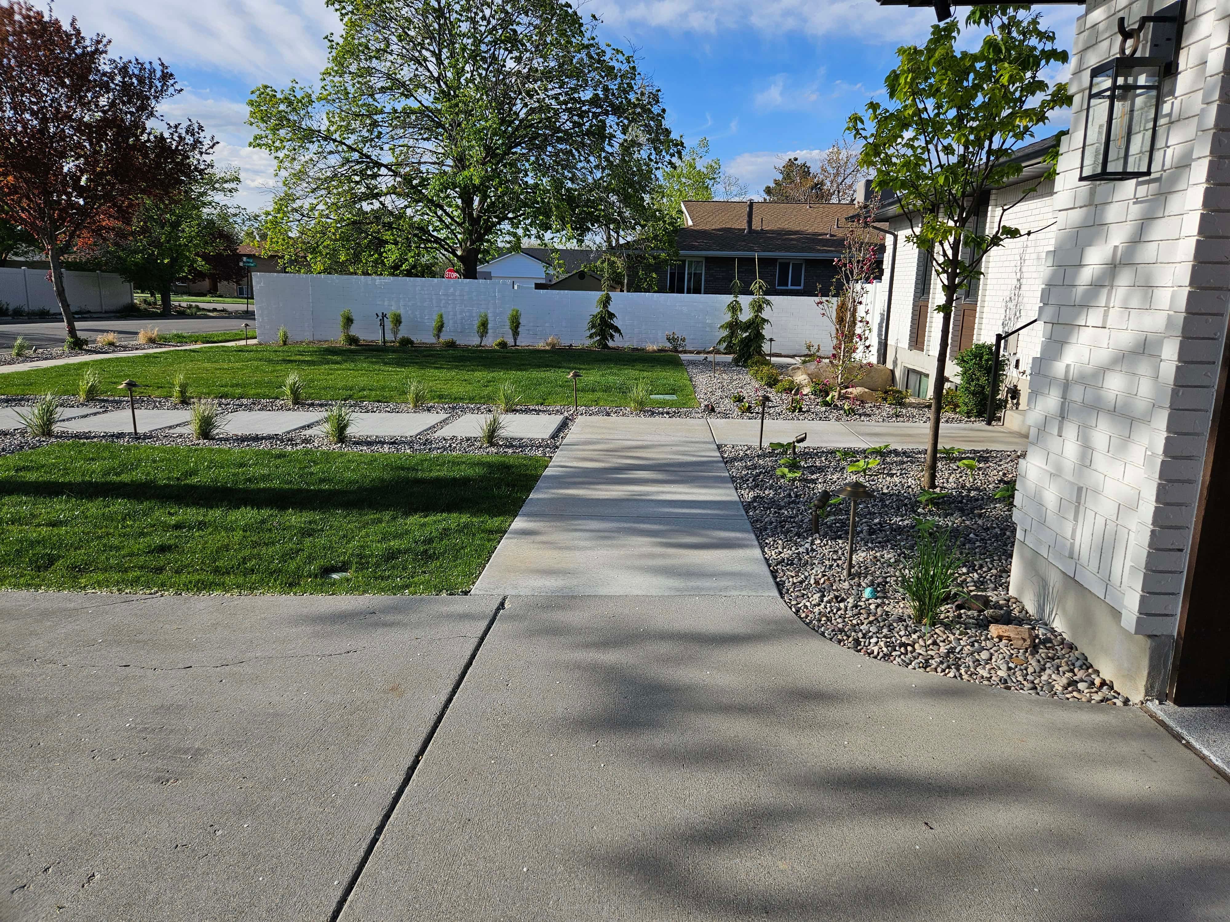 Front yard in South Jordan with a concrete walkway, lush green sod, and landscape plantings.