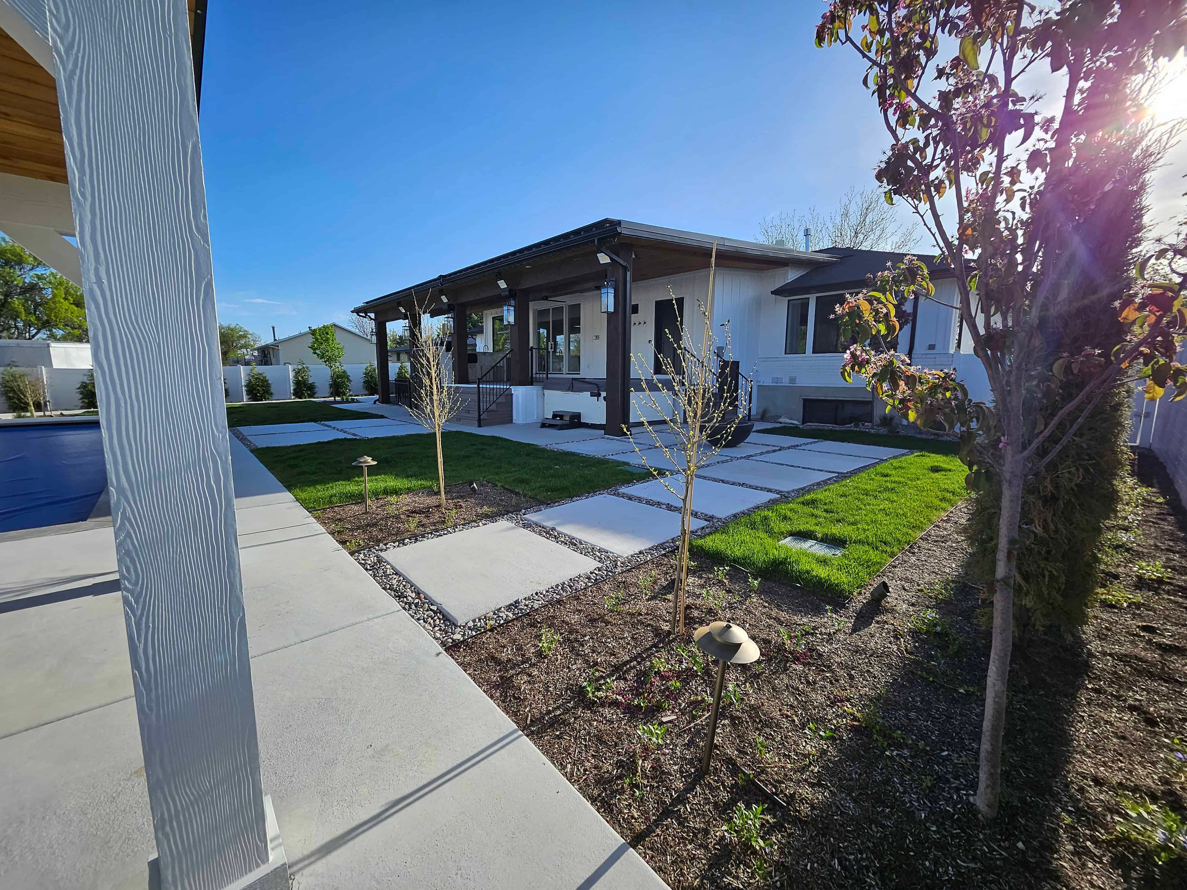 Backyard in South Jordan with modern concrete walkway, fresh sod, and landscape plantings for a clean, contemporary design.