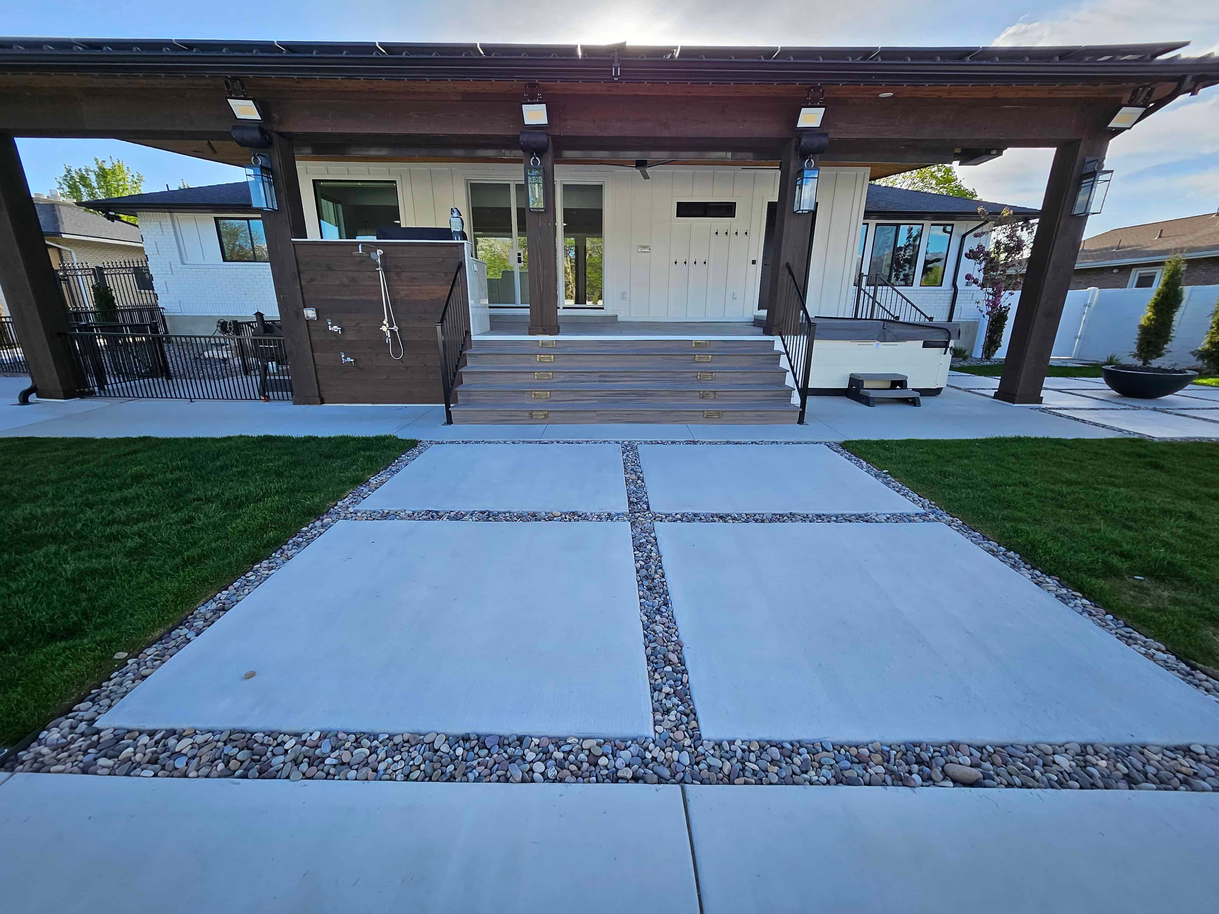 Backyard in South Jordan with large modern concrete squares leading to a back deck and outdoor shower area.