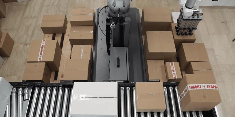 Overhead view of mixed cases of different sizes on a roller conveyor beside an AnyStack robot cell