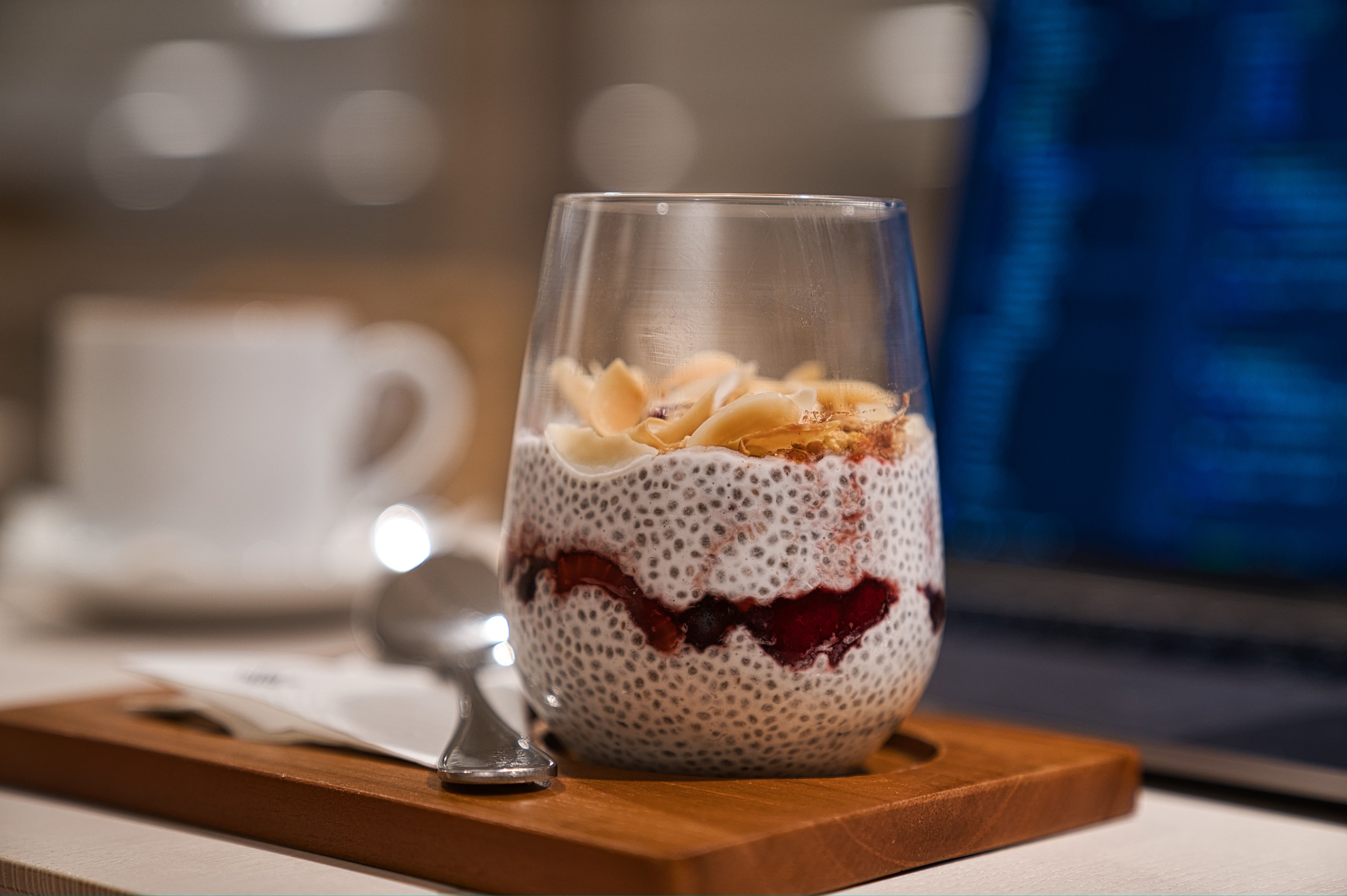 A glass full of Queen Garnet Zesty Chia Pudding sitting on a table with a spoon alongside