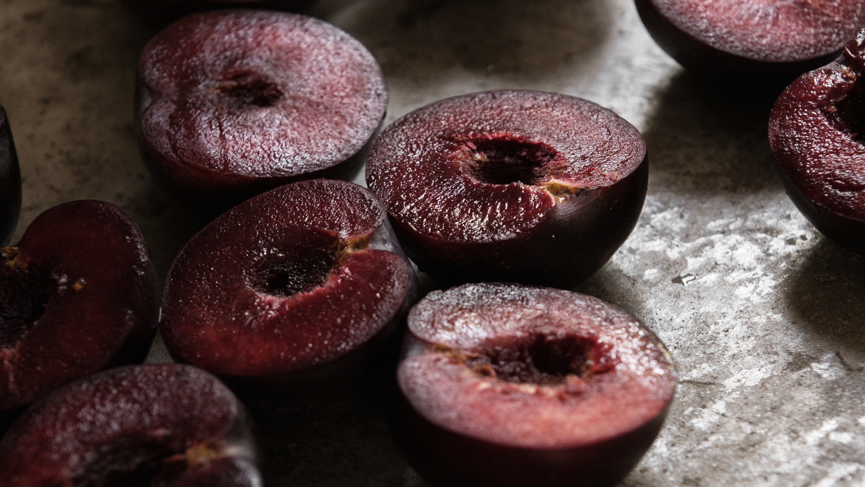 A selection of Queen Garnet plums sliced in half, showing the ripe insides of the fruit