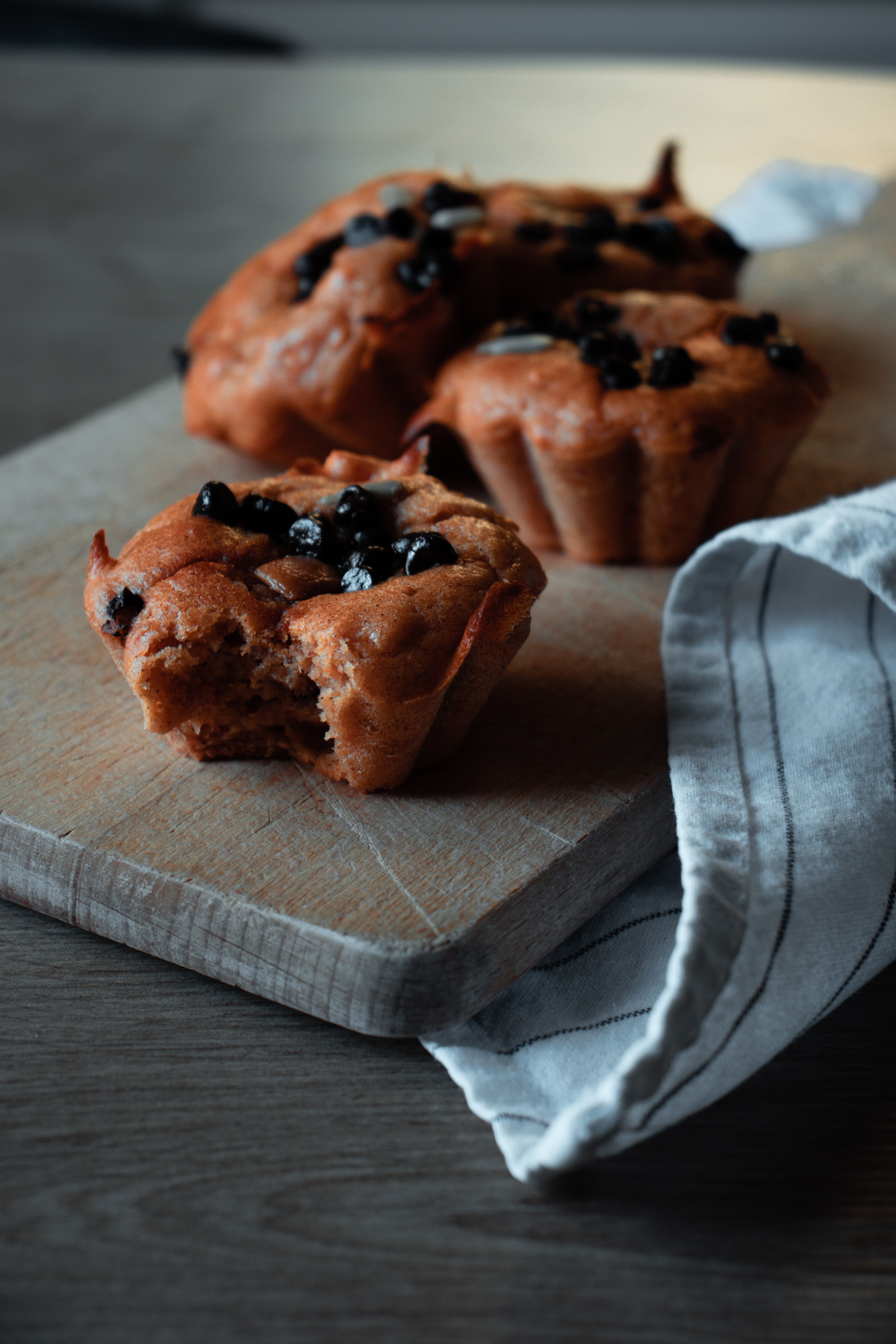 Several Queen Garnet gluten free antioxidant blueberry muffins sitting on a wooden paddle, one with a bite out of the side