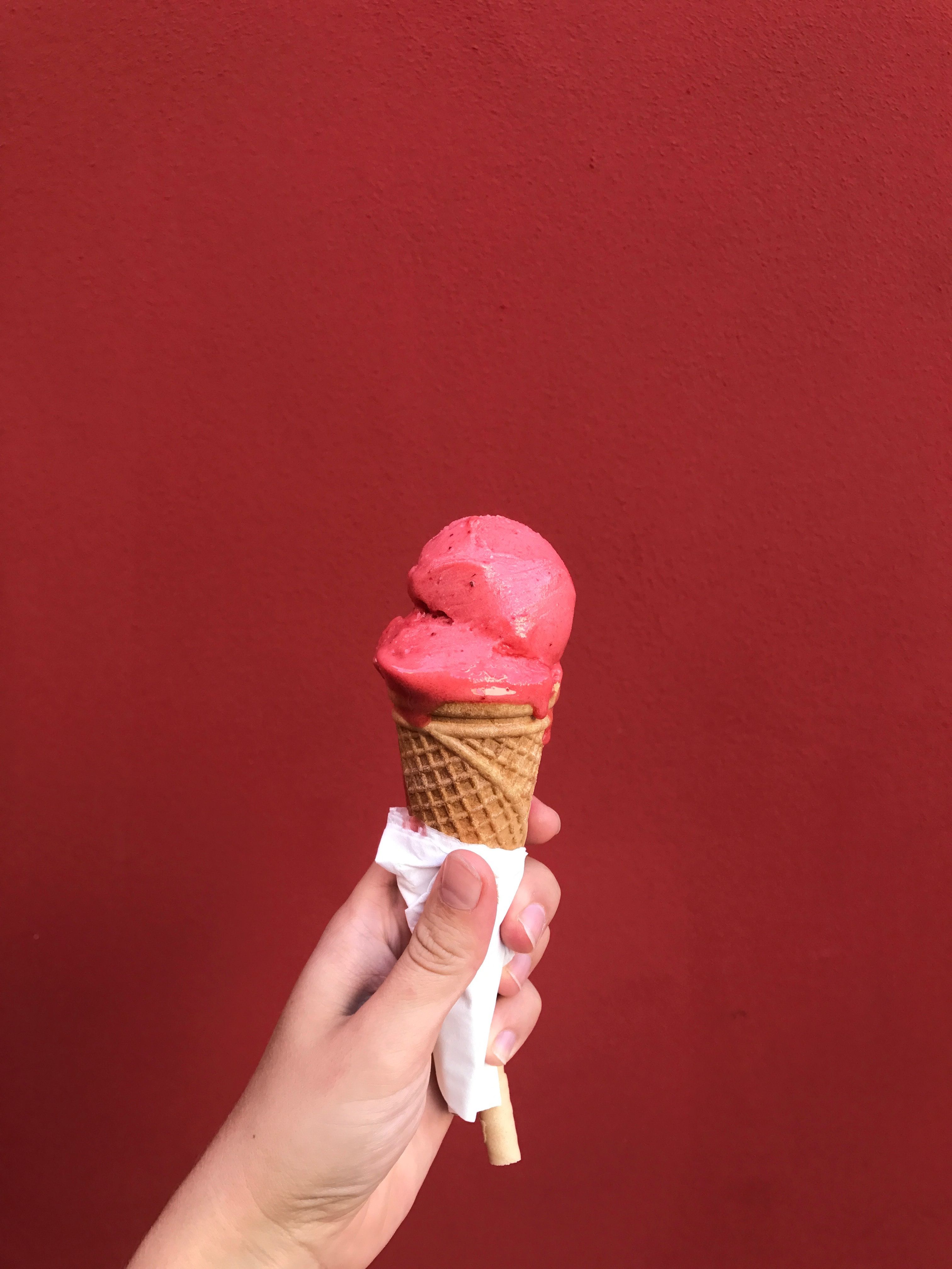 A hand holding a Queen Garnet roasted plum sorbet in a cone