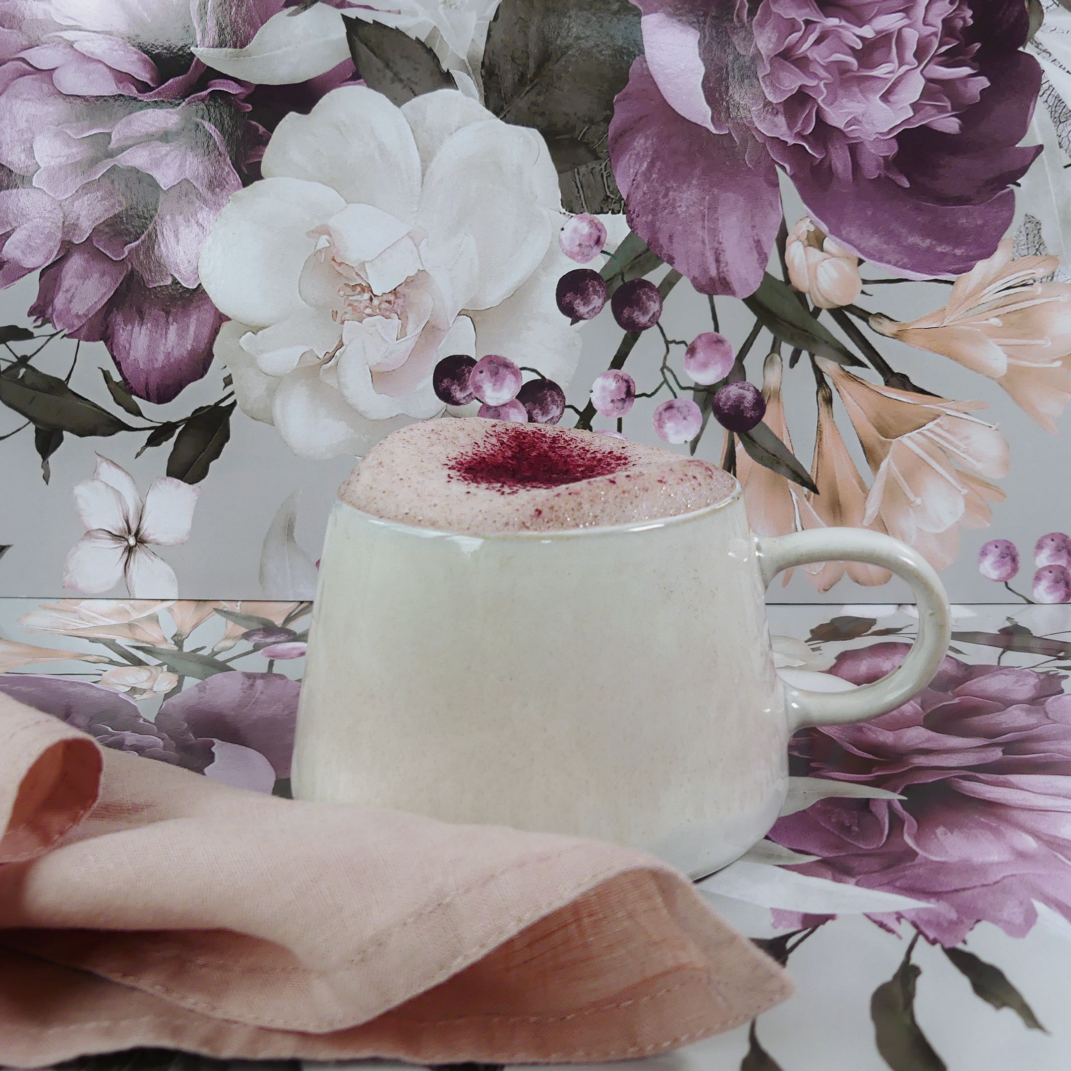 A mug of Queen Garnet Plum latte against a floral backdrop.