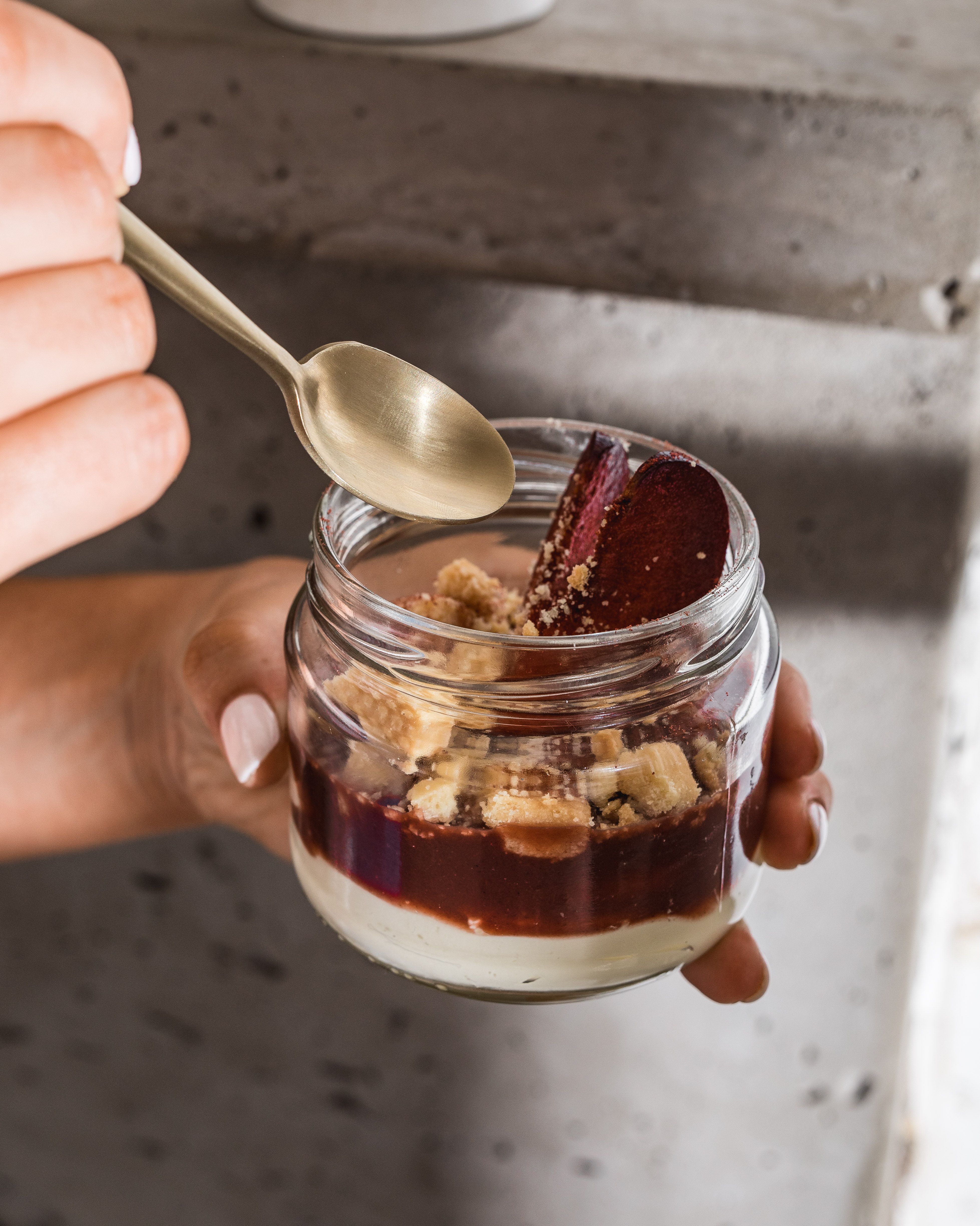A jar of Queen Garnet Plum fool being held, with a spoon about to take out a scoop