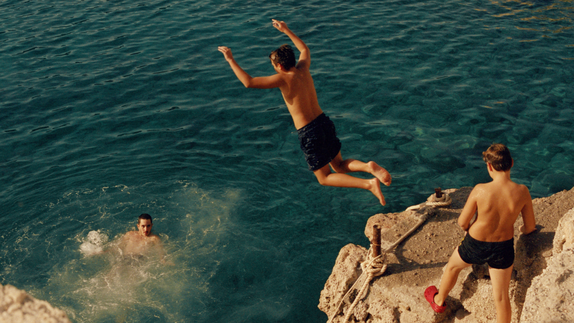 kids jumping off rock into water. Greece