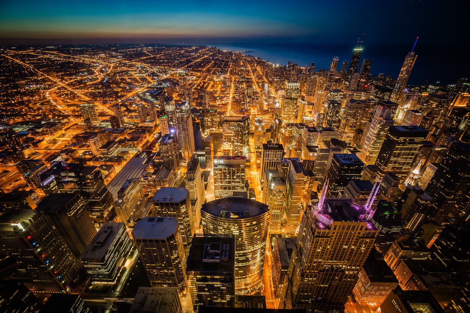 Chicago at night from high above, the illuminated street grid stretching to the horizon. Shot from Willis Tower, the city appears as a dense field of light - the grid that made Chicago the city it became.