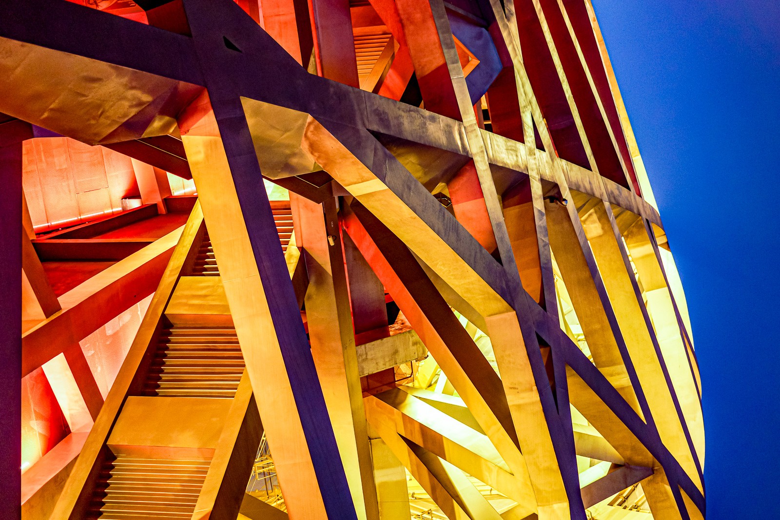 The Bird's Nest in golden light, the steel latticework taking on a warm amber tone. The same building, a different reading - the material responding to what the sky does, the architecture changing without moving.