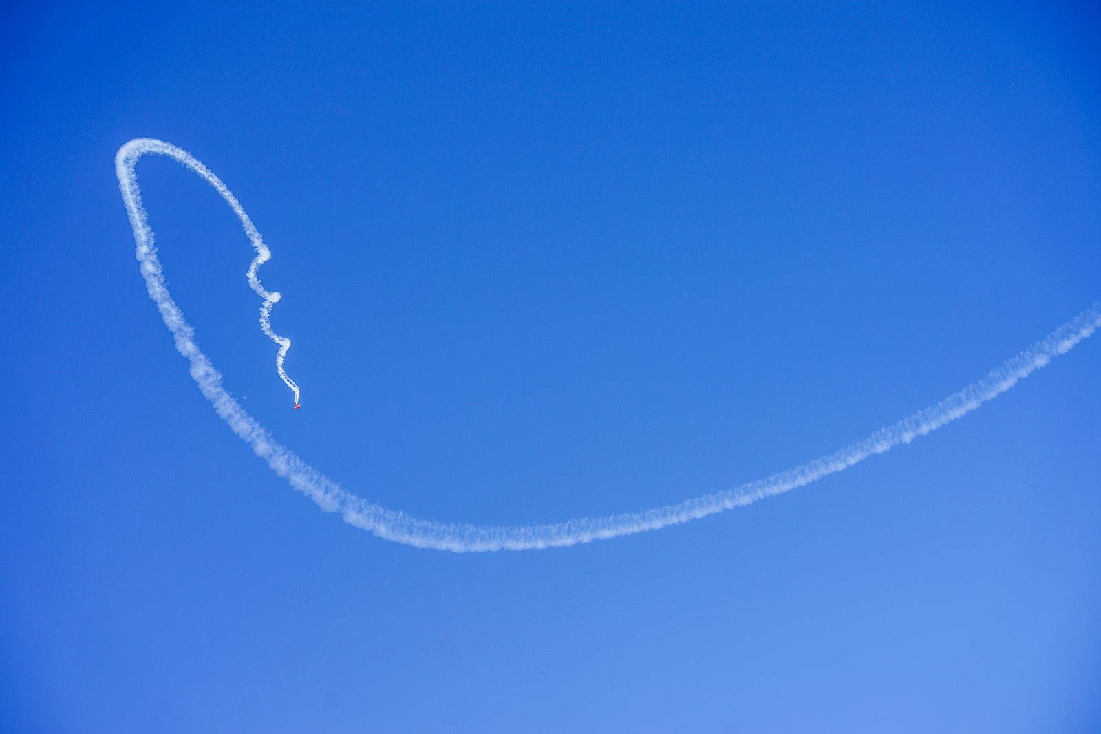 A single aircraft contrail curving in a tight spiral across a cloudless California sky. The white arc dissolves slightly at the edges, the sky below it perfectly empty - a line drawn briefly in the air, then gone.