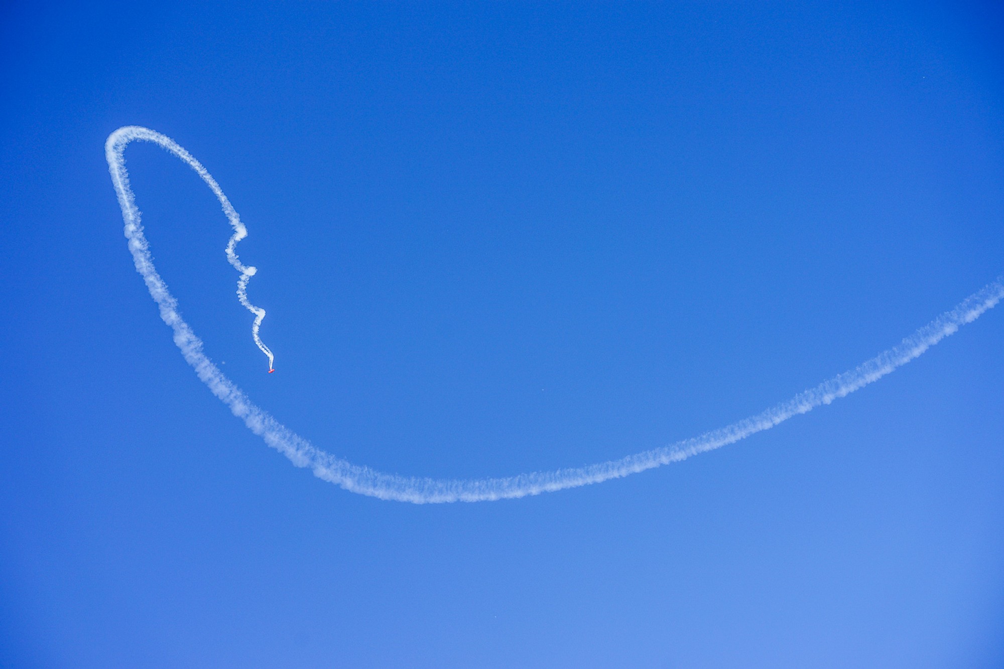 A single aircraft contrail curving in a tight spiral across a cloudless California sky. The white arc dissolves slightly at the edges, the sky below it perfectly empty - a line drawn briefly in the air, then gone.