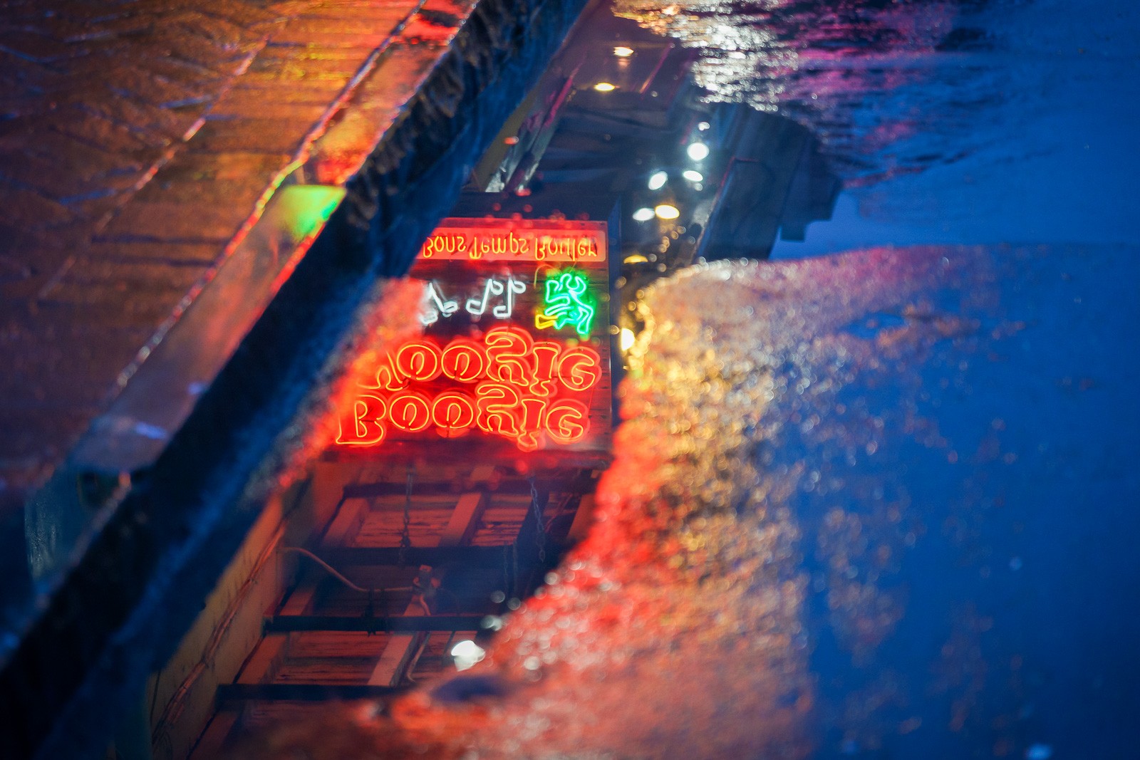 Looking down at a New Orleans street corner at night, the neon sign below casting its name in light across the pavement. An image about the city's particular relationship with the hours after midnight.